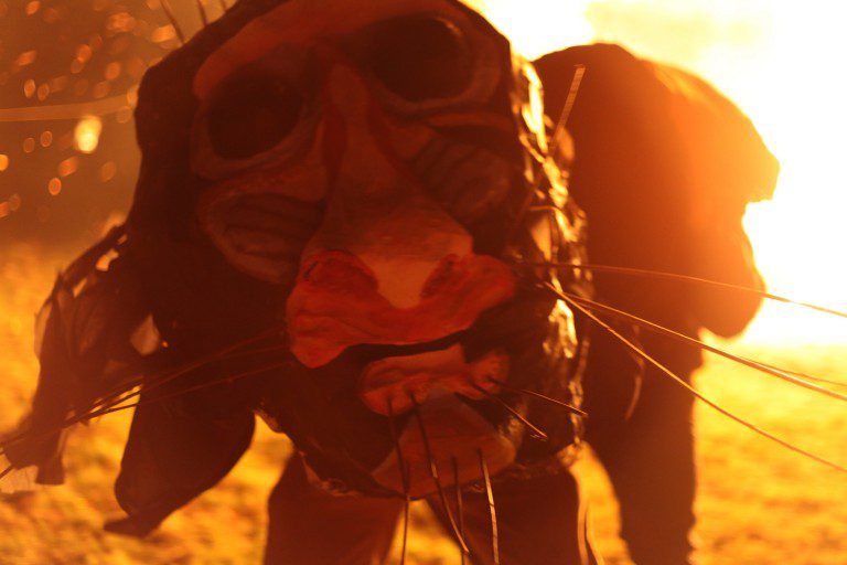Close-up of a person wearing goggles and a mask, with a bright, fiery background, possibly during a wildfire or intense blaze.