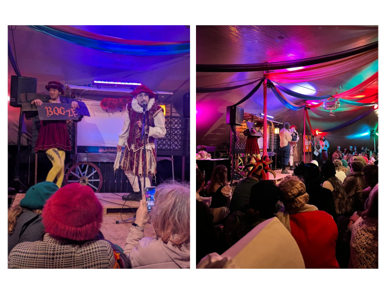 Stage performance with two actors in costumes, one dressed as a pirate with a beard and one holding a sign, in a decorated tent with colorful lighting and an audience watching.