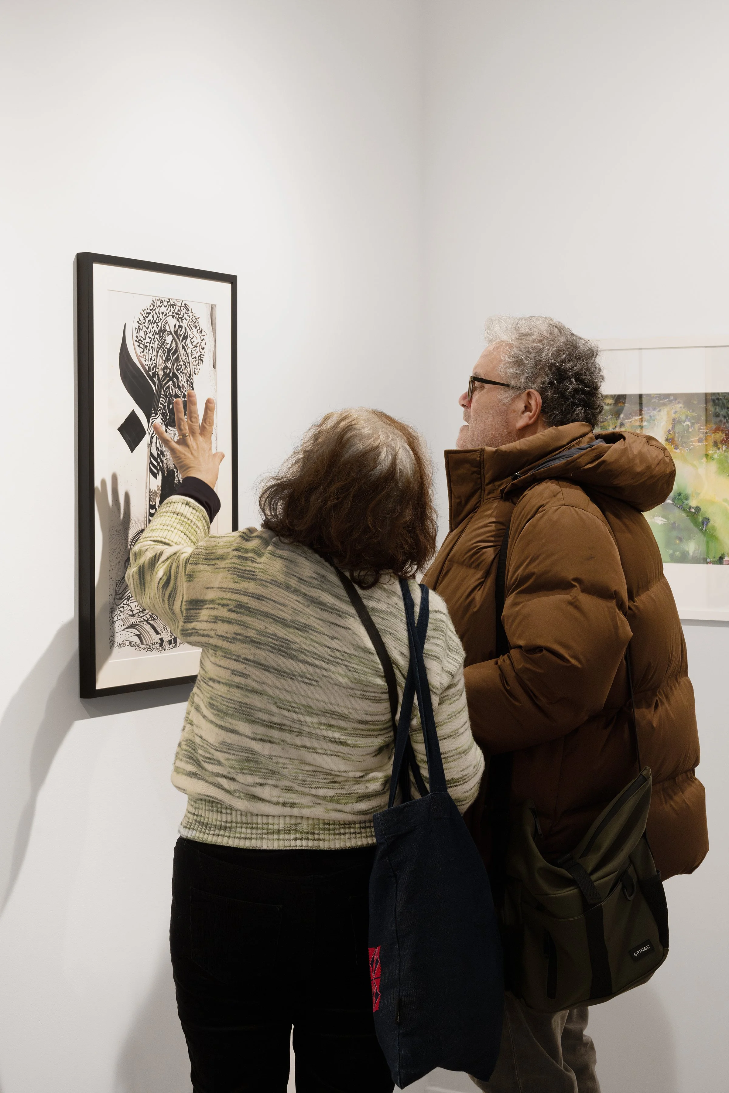 Two people looking at a framed artwork in an art gallery, with one person pointing at the artwork.