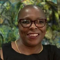 Close-up of a woman with short hair, wearing glasses, smiling, with a nature background.