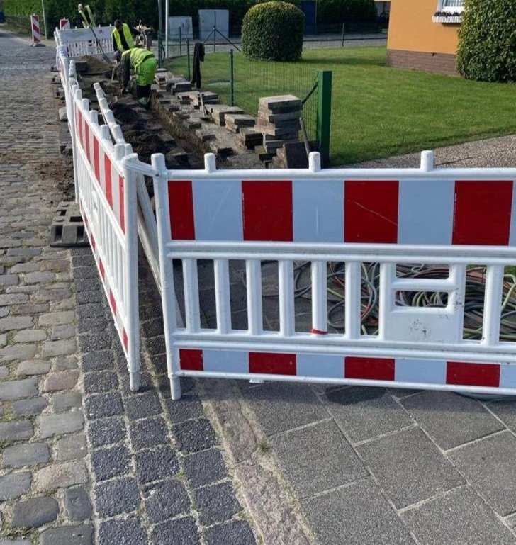 Road construction site with workers installing bricks and a temporary safety barrier and fencing.