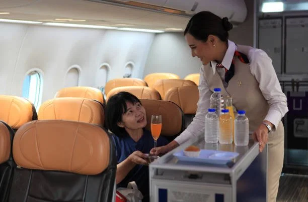 A flight attendant serving a passenger a drink on an airplane.