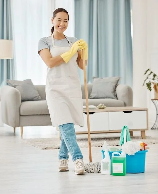 A woman in casual clothes and yellow cleaning gloves mops the floor in a living room with a blue cleaning bucket, spray bottles, and cleaning supplies nearby.