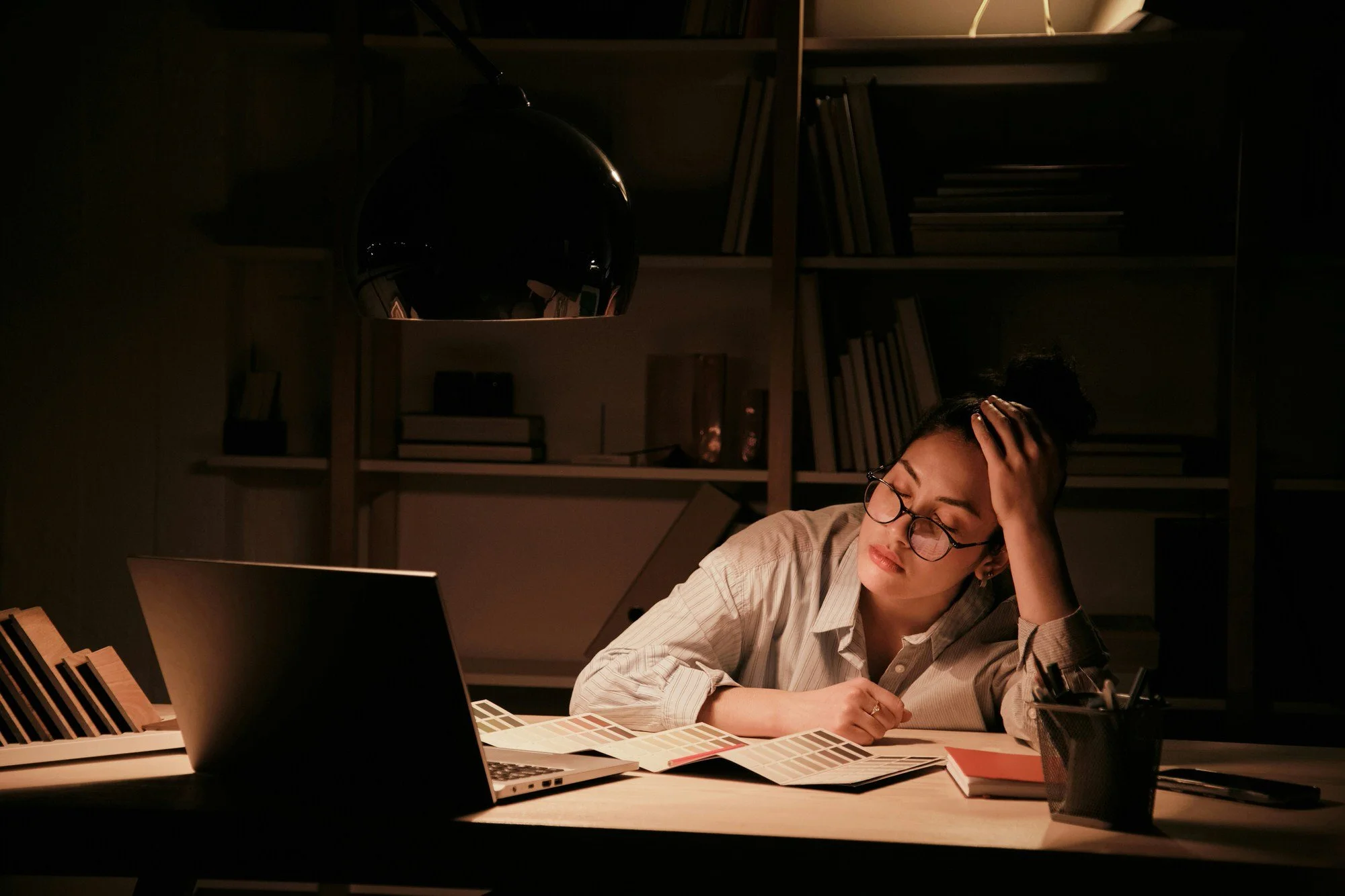A woman looking tired and frustrated, sitting at her desk in the dark
