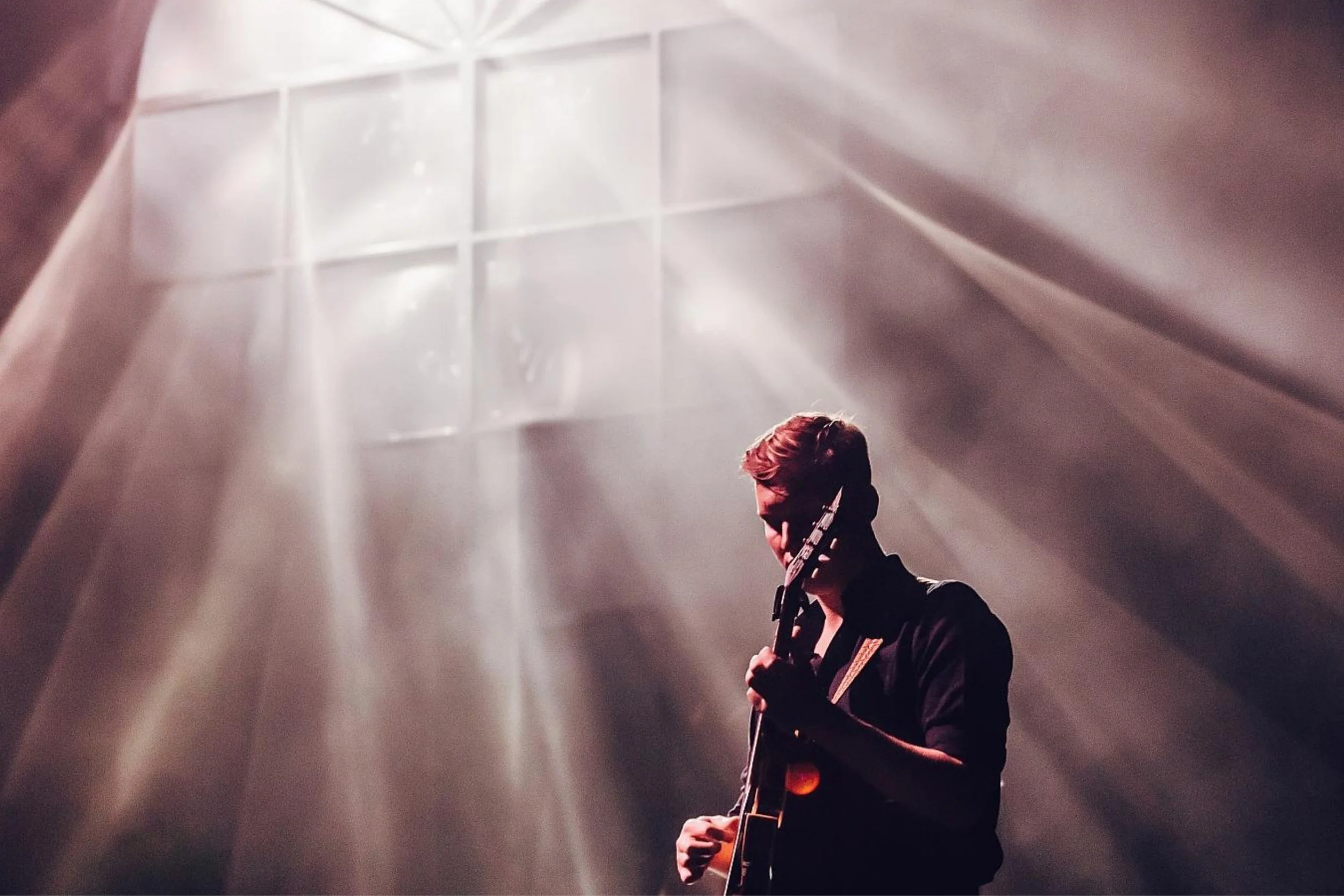 A guitarist performing in beams of light streaming through a window frame, from Cate Carter’s portfolio.