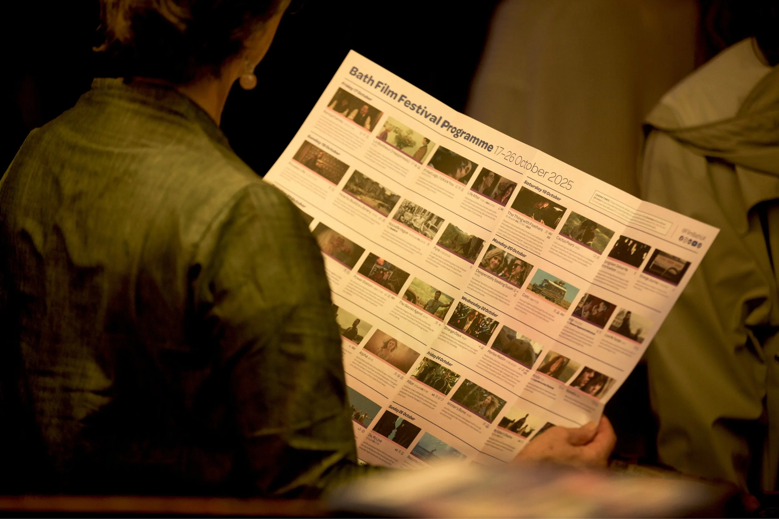 A guest holding the Bath Film Festival programme, showing film listings with stills.