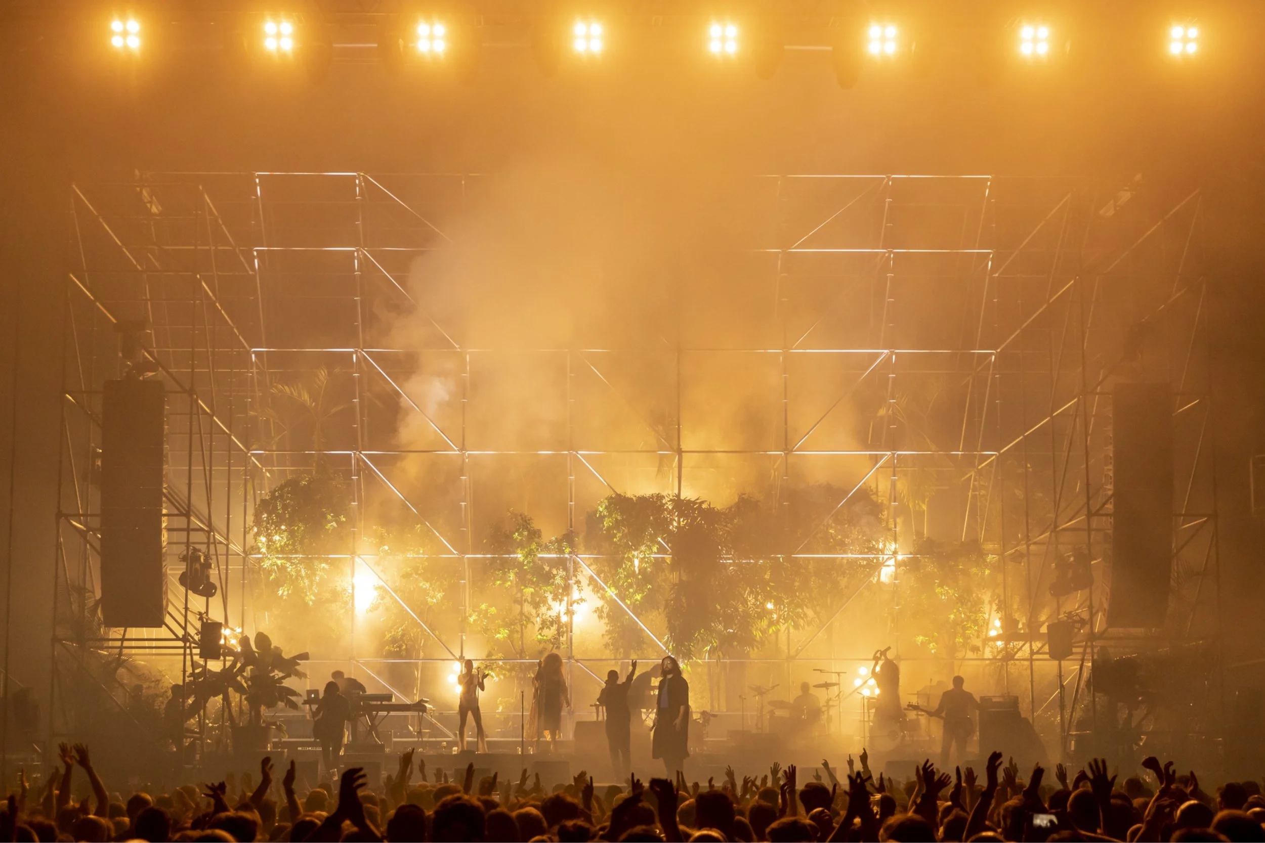 A band performing on a scaffold stage filled with plants and golden haze, from Cate Carter’s portfolio.