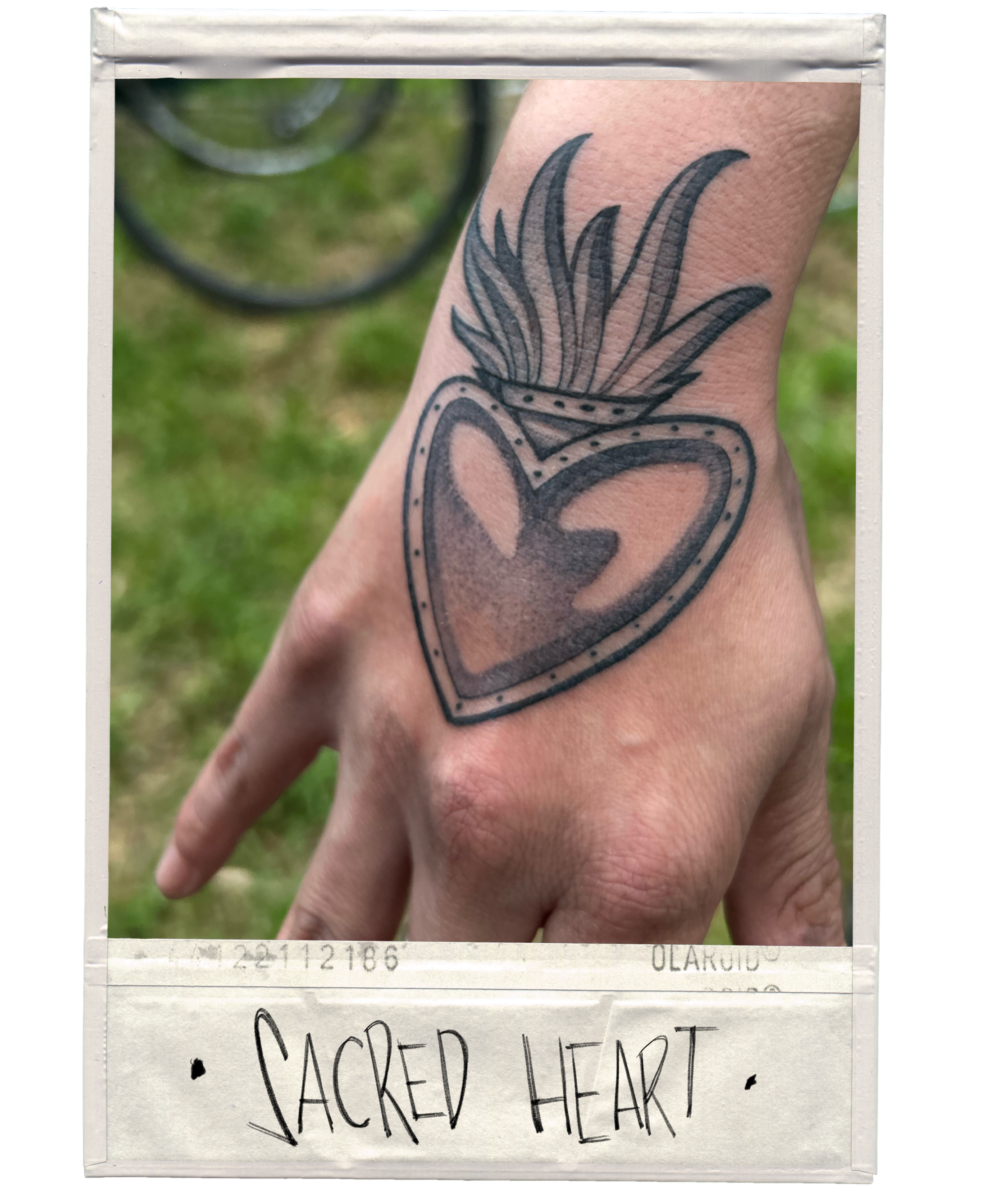 A tattoo on a person's hand depicting a heart with a flame on top, outlined with dots and shading, labeled 'Sacred Heart' at the bottom.