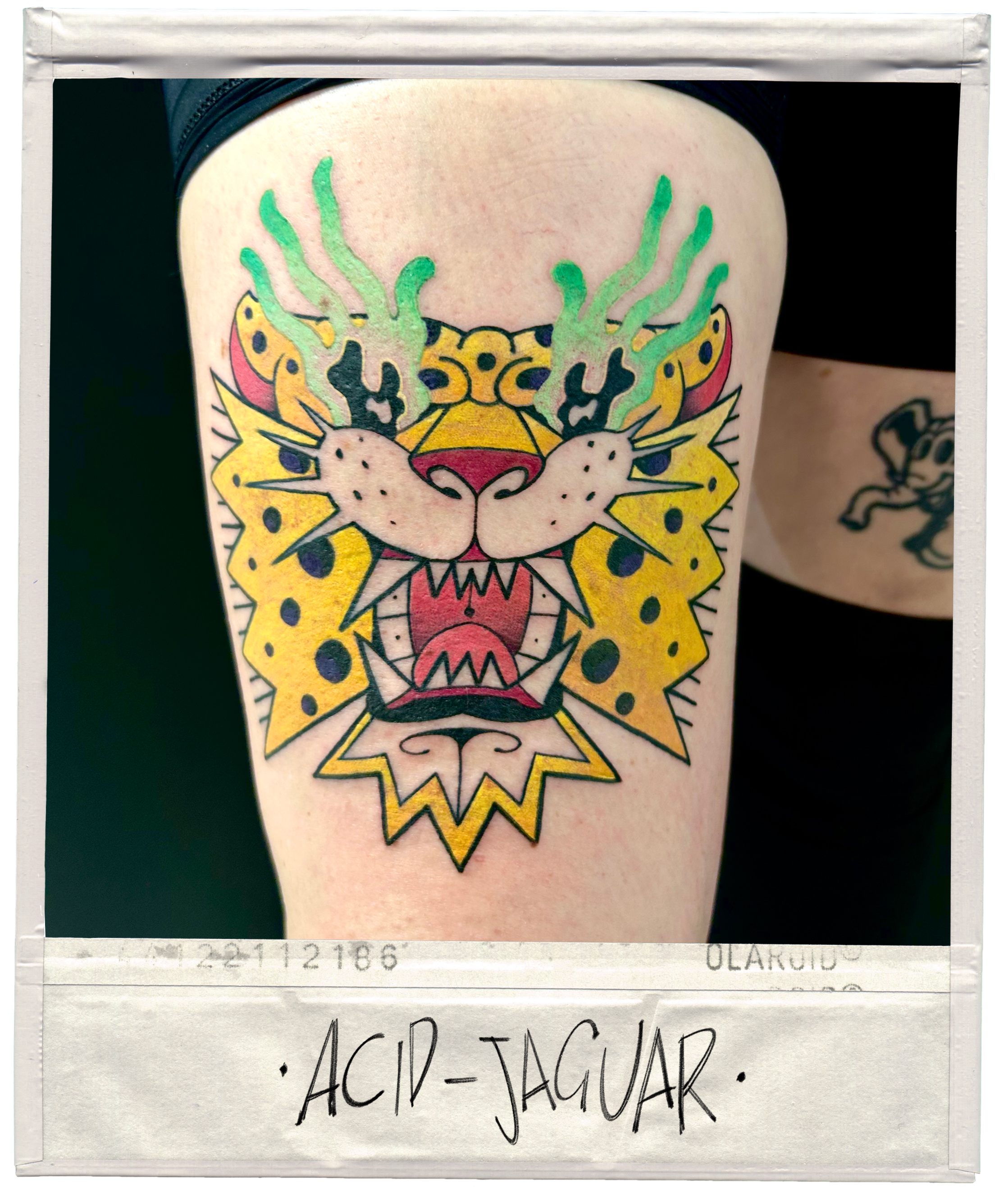 Tattoo of a colorful, stylized jaguar's face with green flames or smoke coming from its forehead, on a person's upper arm.