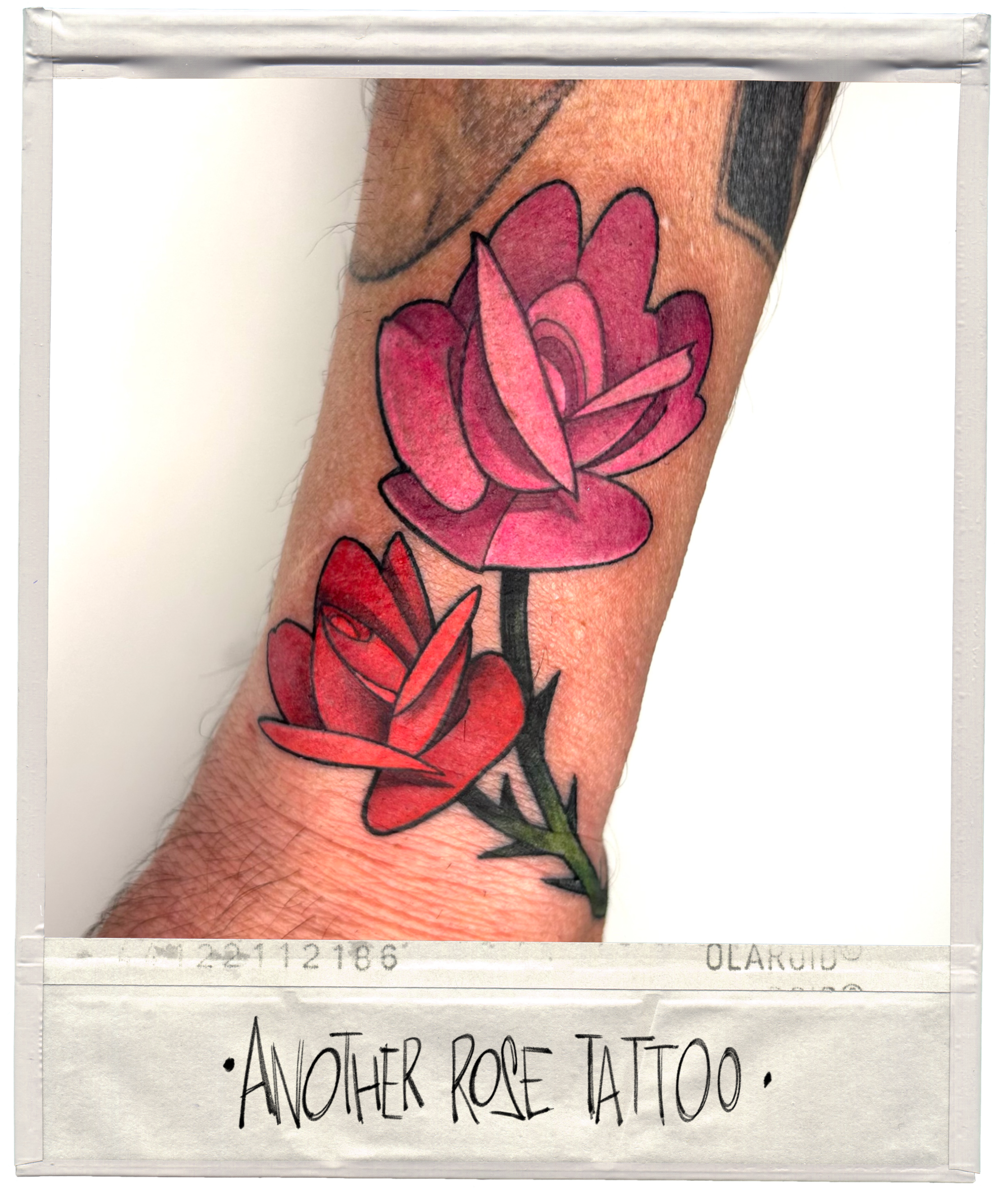 Colorful tattoo of two pink and red roses on a person's forearm, with a white border at the bottom that reads 'Another Rose Tattoo'.