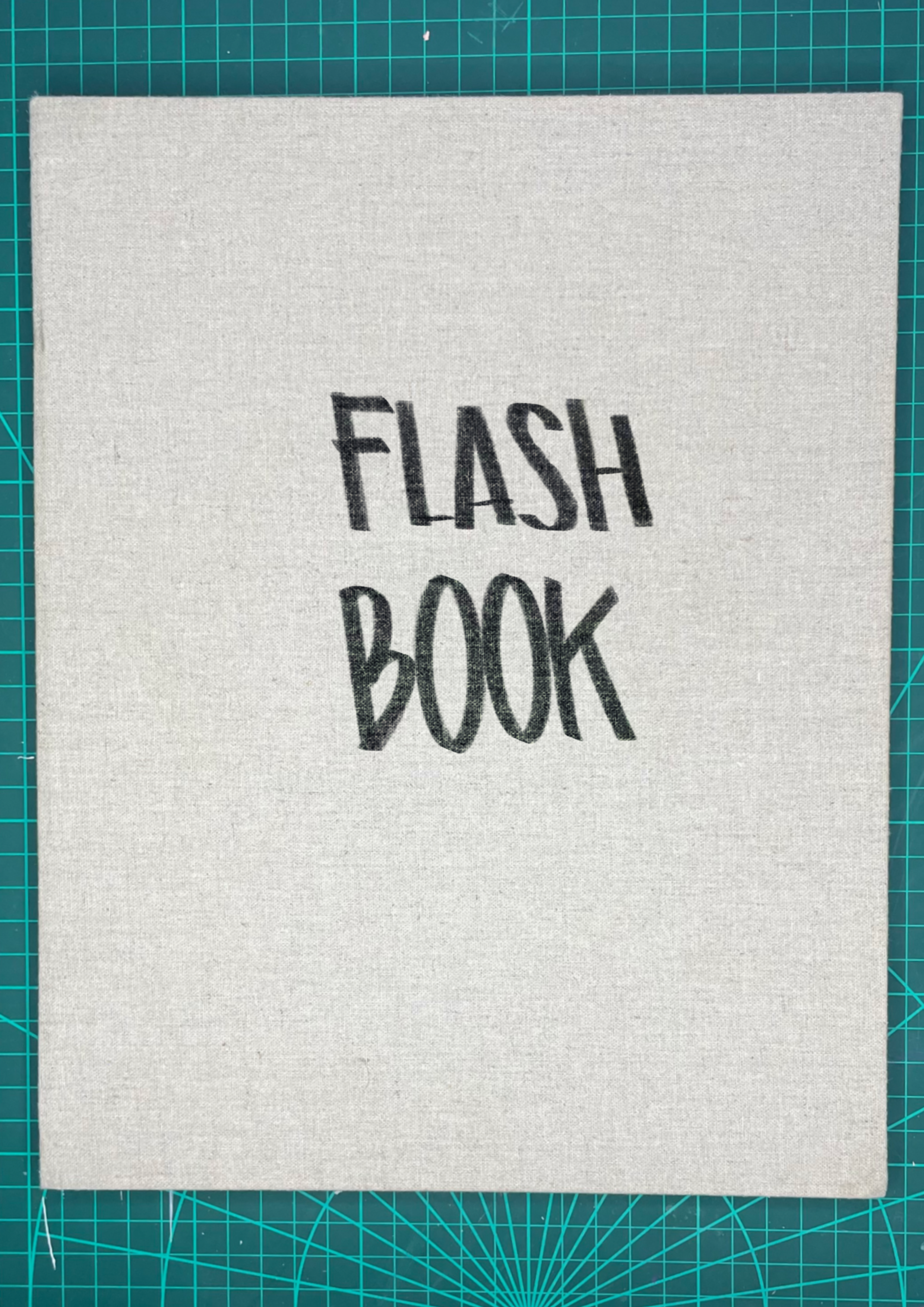 A notebook with the words "FLASH BOOK" written in large black letters on its cover, placed on a green cutting mat.