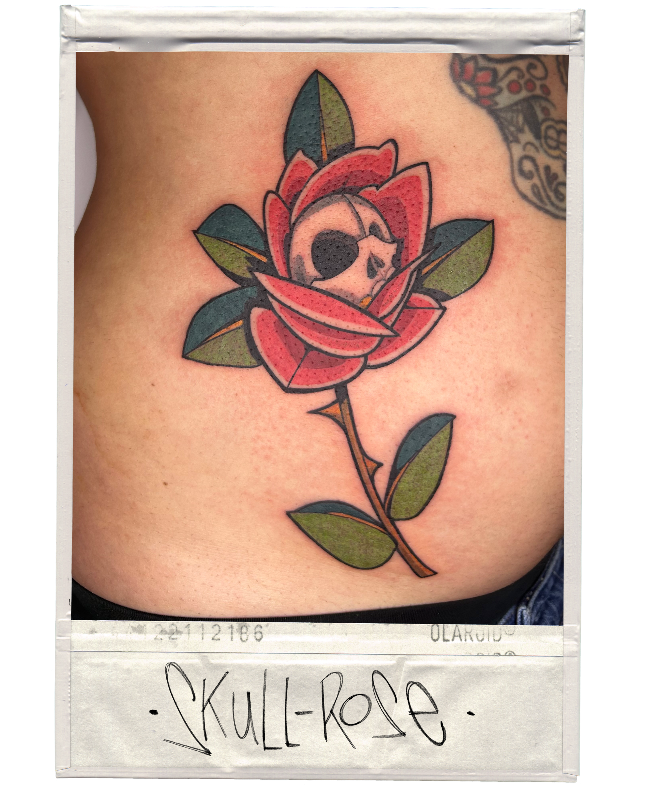 Tattoo of a skull inside a red rose with green leaves on skin.