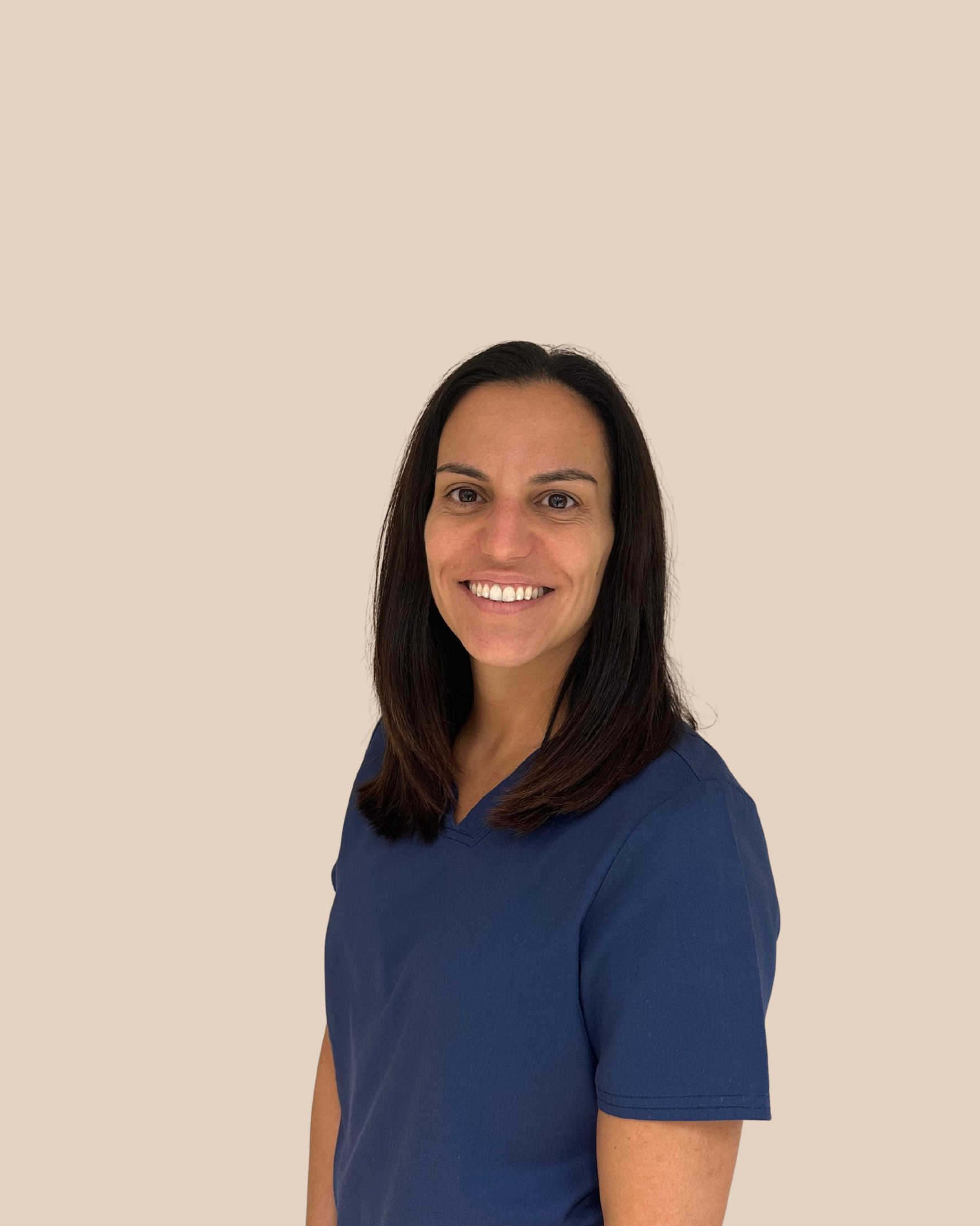 Mujer con cabello largo y oscuro y sonrisa, vestida con uniforme azul, fondo beige.