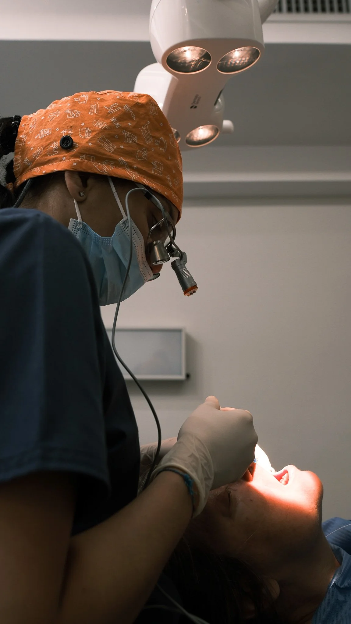 Una dentista enmascarada y con gafas trabaja en la boca de una paciente en una intervención dental en un consultorio.