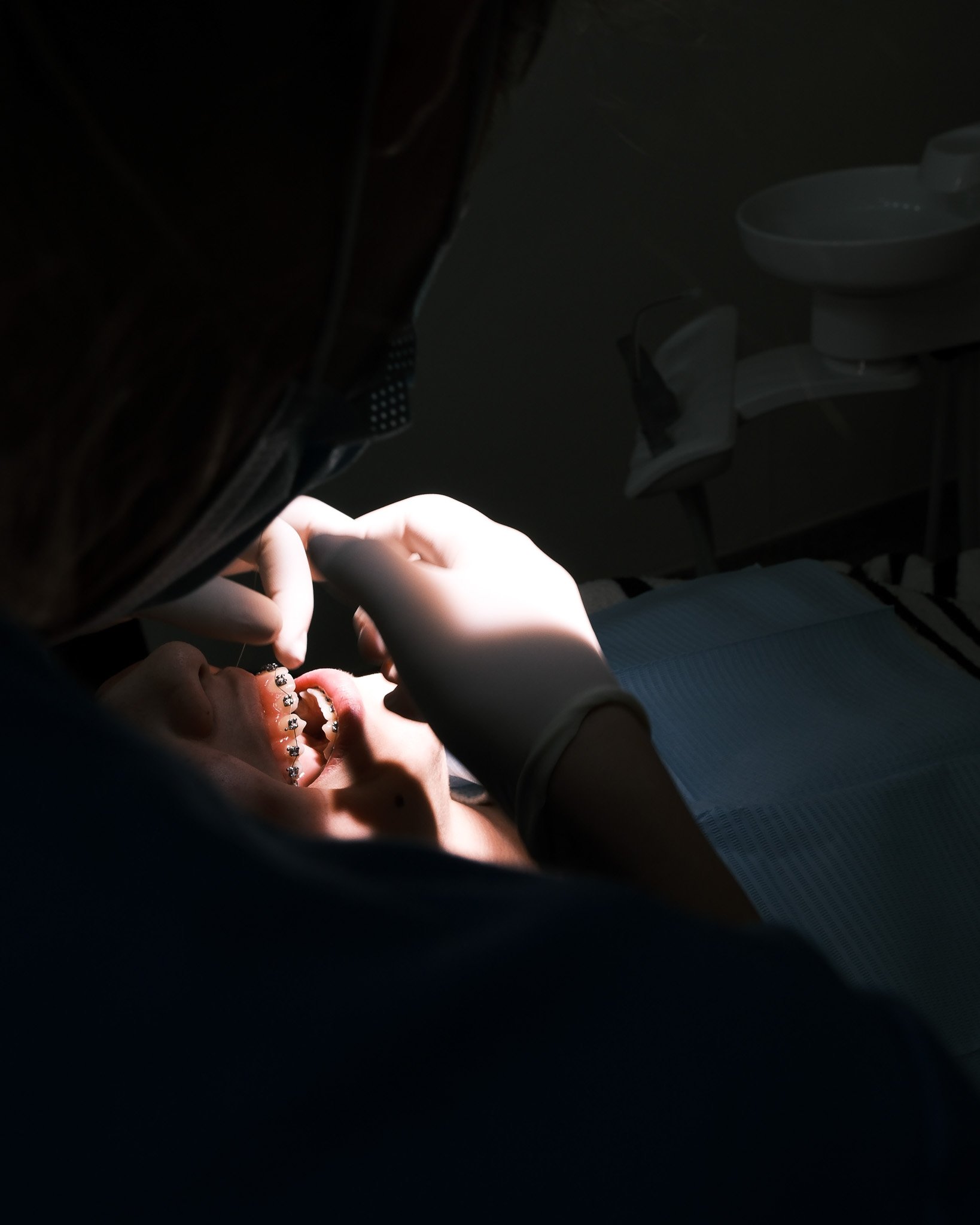 Un dentista atendiendo a un paciente en un consultorio, el paciente tiene brackets en los dientes.