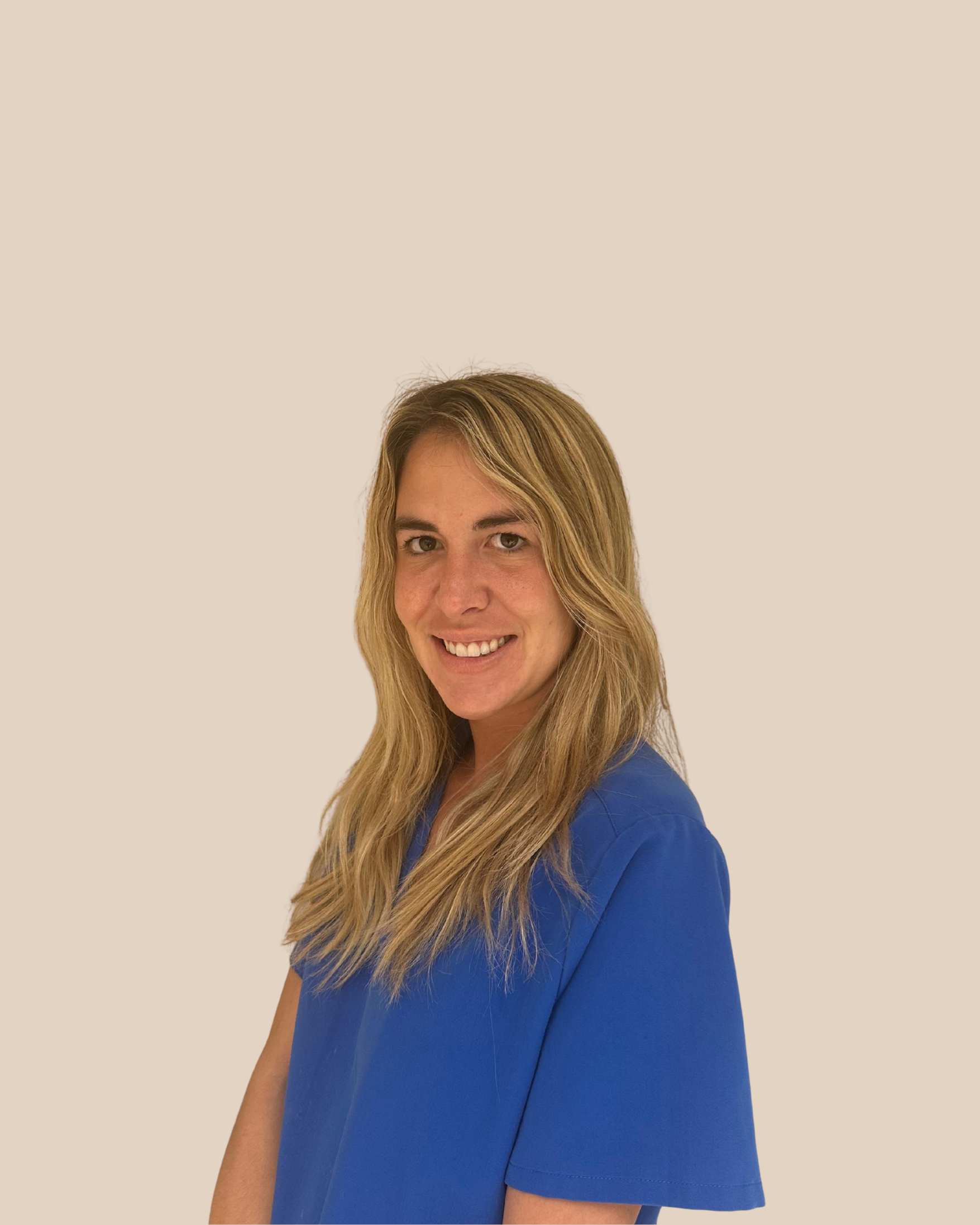 Retrato de una mujer sonriendo, lleva uniforme azul, fondo beige liso.