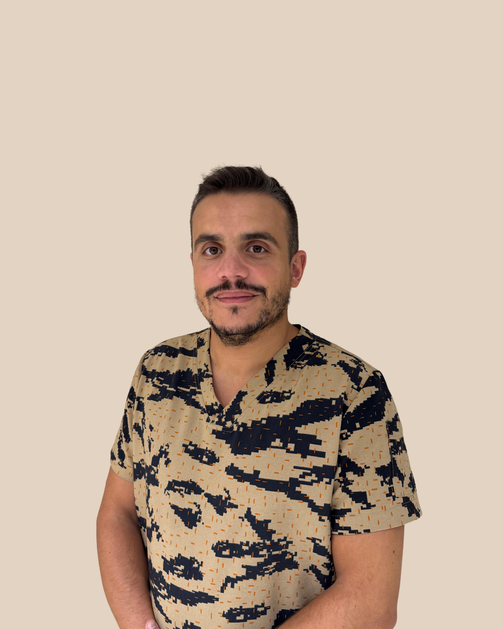 Hombre con barba y camiseta de camuflaje sentado frente a fondo beige.