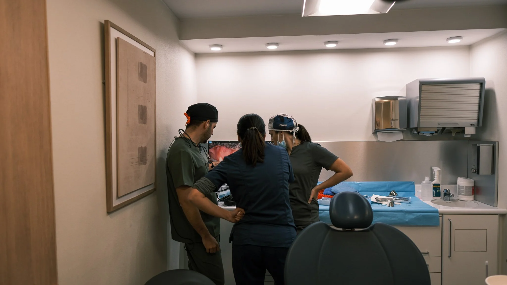 Tres profesionales de la salud en una consulta médica en un quirófano o sala de procedimientos, revisando una pantalla de monitor médico.