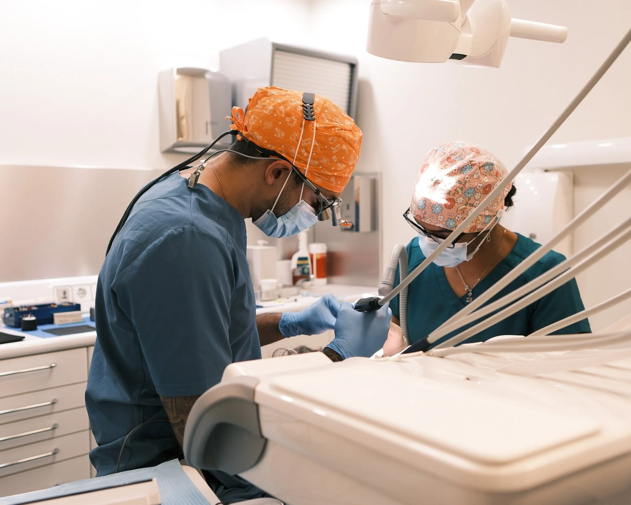Dos profesionales médicos en un procedimiento, uno con un bisturí y ambos usando mascarillas y batas, en un entorno clínico.