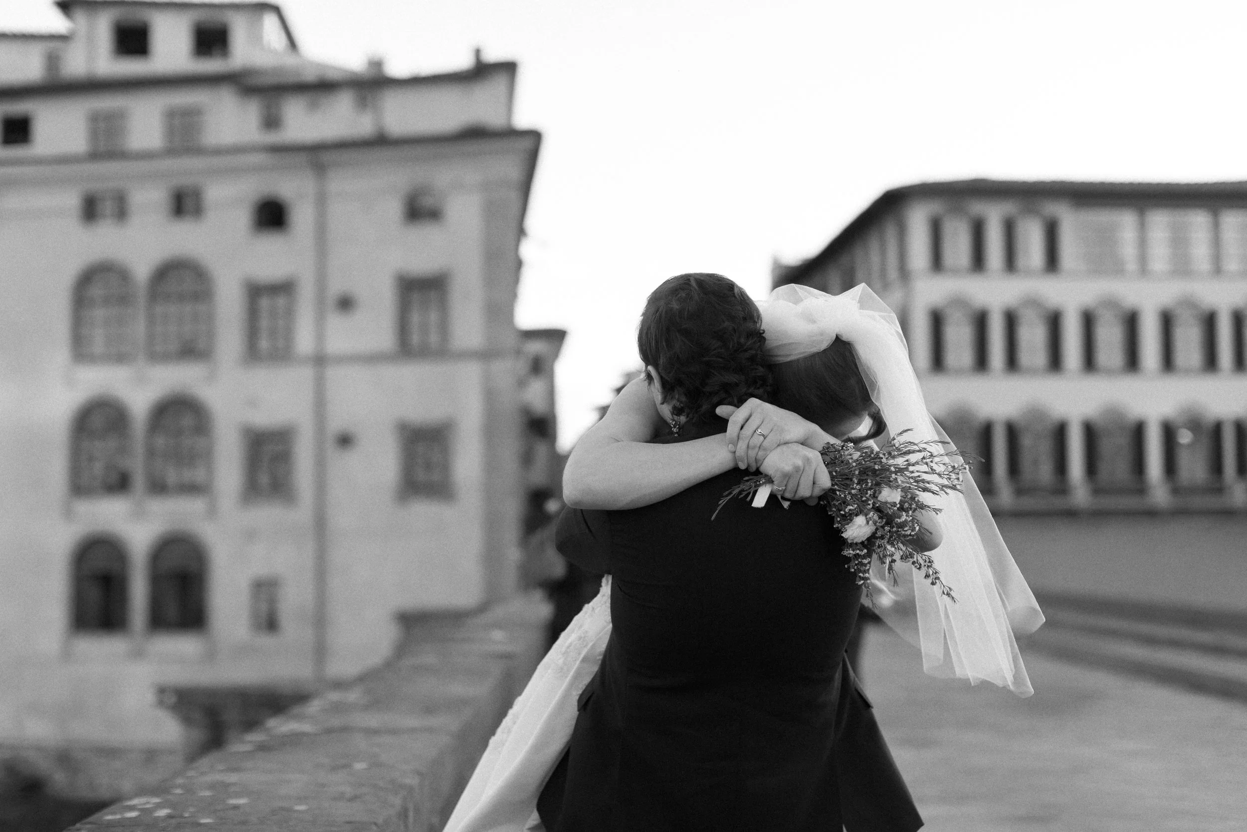A bride and groom embrace on iconic bridge in Florence, Italy. Destination wedding portrait shoot after ceremony.