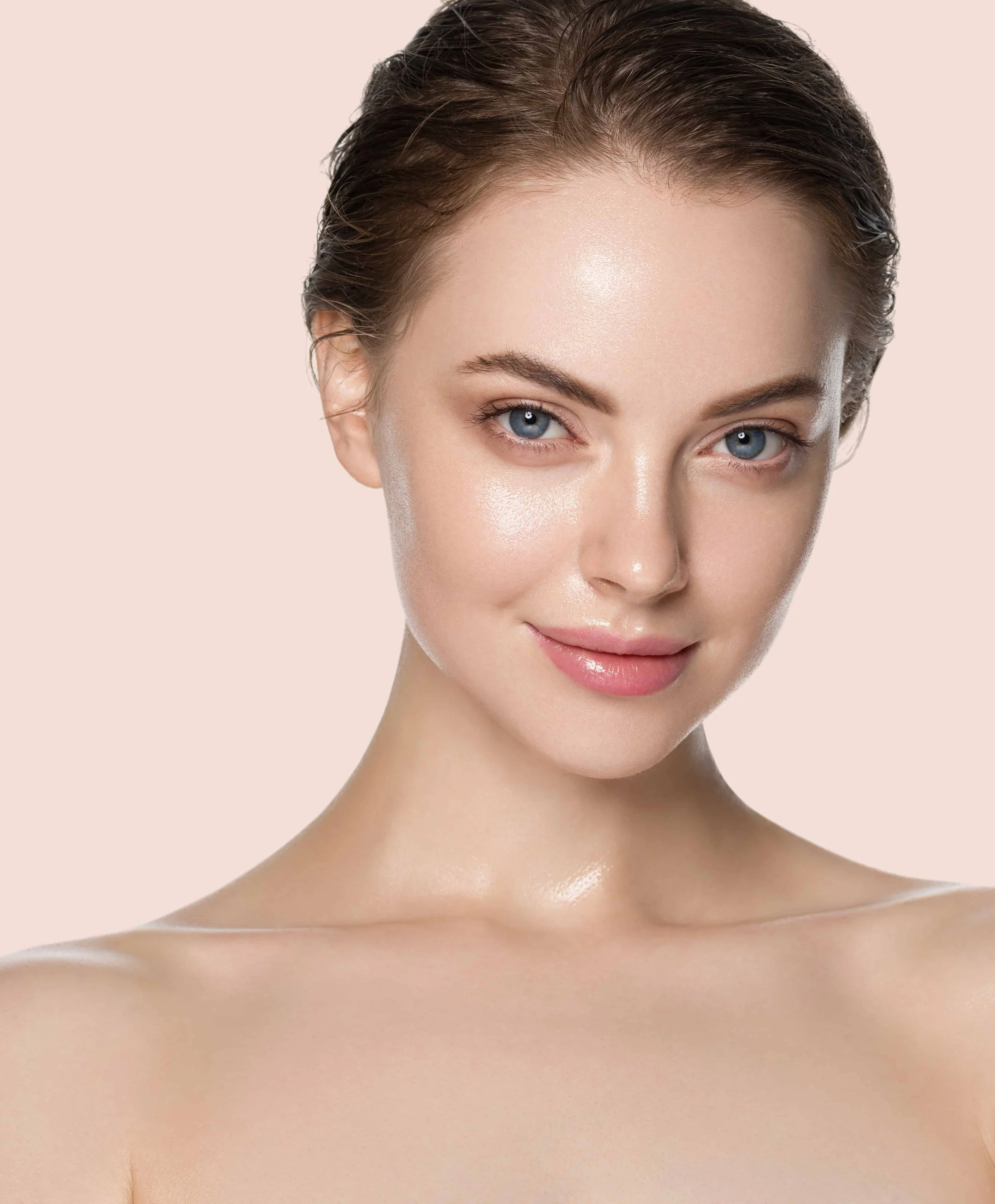 Nærbilde av et smilende kvinnelig ansikt med bare skuldre, glødende hud og lys blå øyne mot en lys rosa bakgrunn.