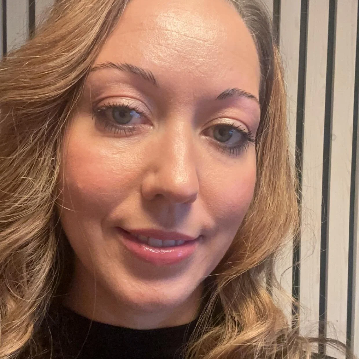 Nærbilde av en ung kvinne med lyst, krøllete hår og smil, som ser mot kamera.