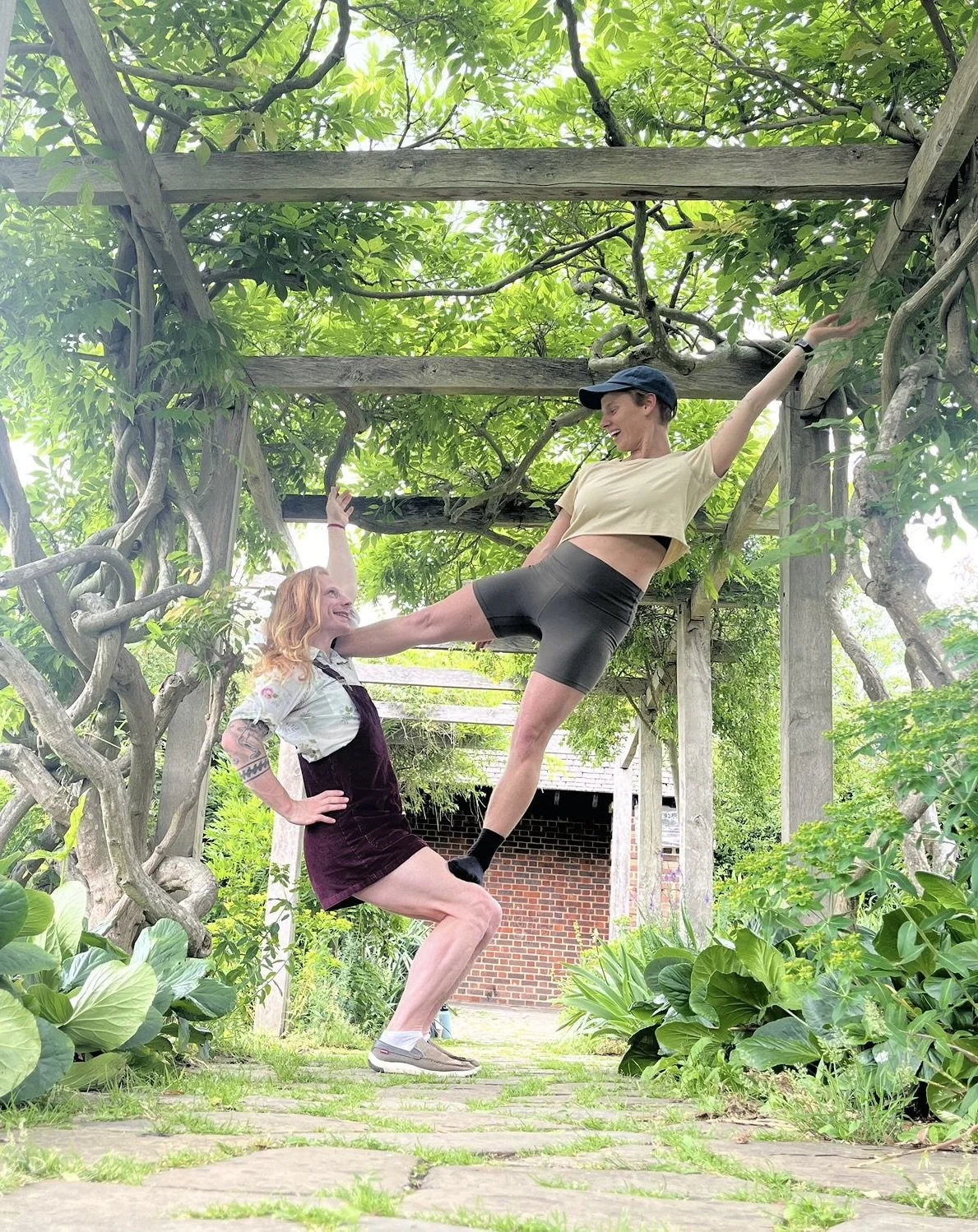 joey and a non binary person doing a flag (acrobatic position) in a pergola surrounded by greenery