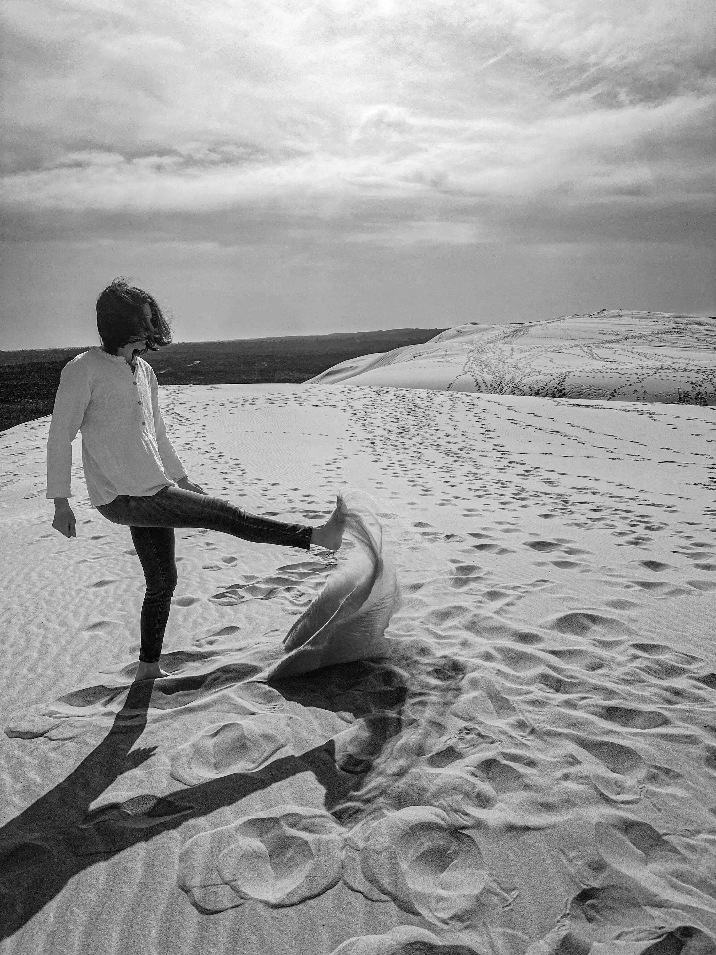 Gironde. Bassin d'arcachon. Bordeaux  Atelier estime de soi méthode Monbourquette accompagnement. Une personne debout dans un désert de sable, levée une jambe, avec des empreintes de pas autour, un ciel nuageux en arrière-plan.