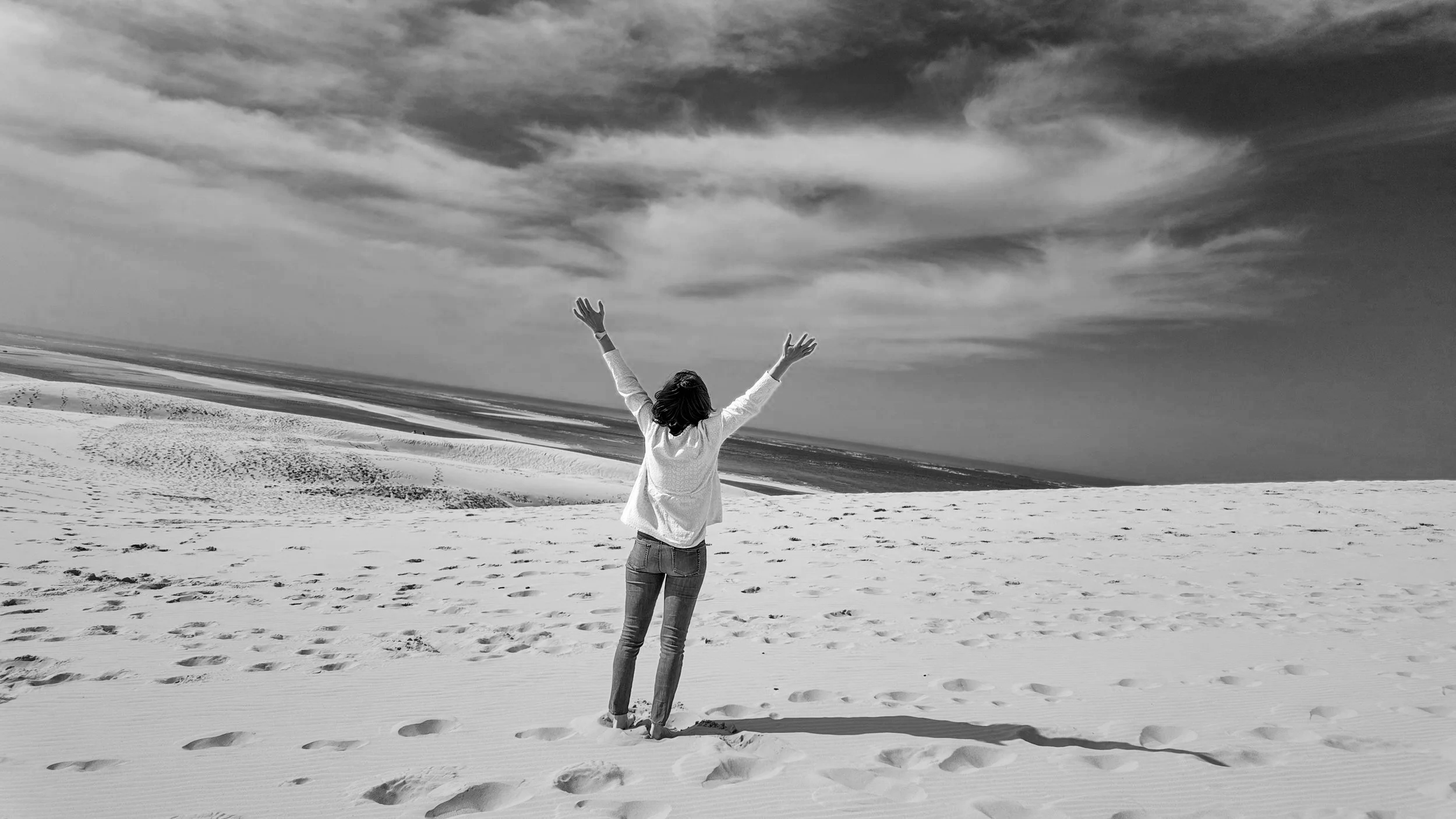 Libération émotionnelle estime de soi praticienne méthode Monbourquette. Une personne debout sur une plage de sable, levant les bras vers le ciel, avec un ciel nuageux en arrière-plan. Dune du Pilat. Gironde. Bassin d'arcachon. Bordeaux