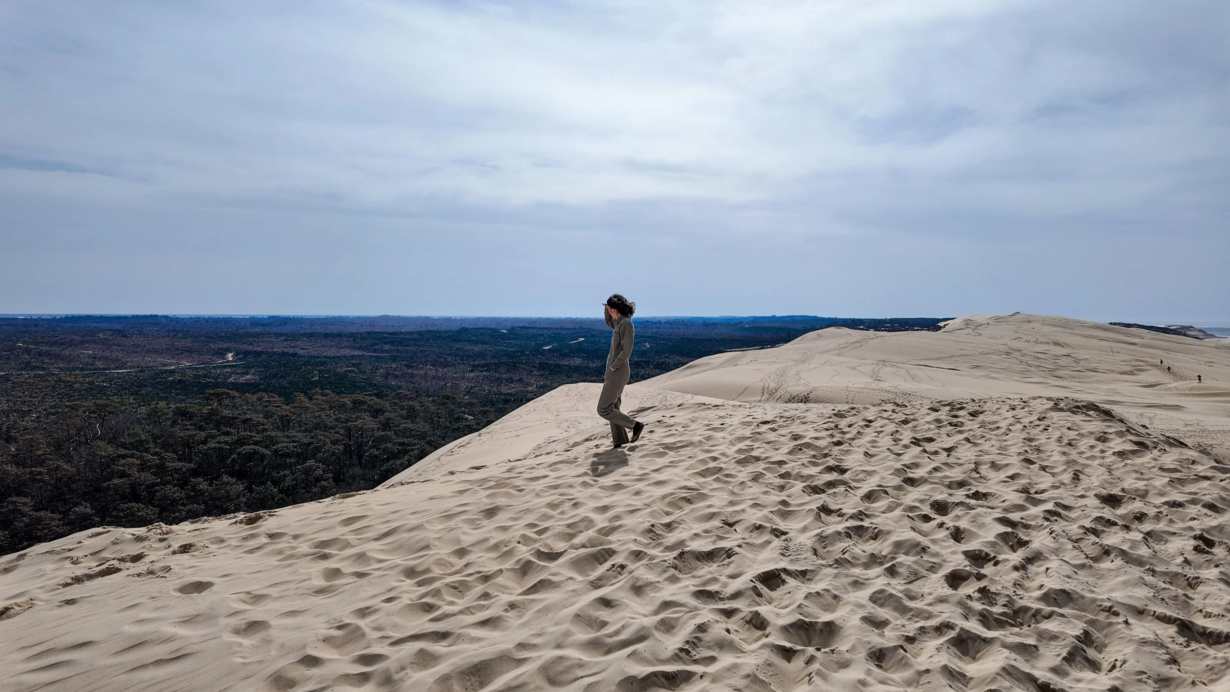 Accompagnement estime de soi méthode Monbourquette éveloppement personnel.Une personne debout sur des dunes de sable dans un désert ou une zone désertique, avec un ciel nuageux et une forêt au loin.Dune du Pilat. Gironde. Bassin d'arcachon. Bordeaux