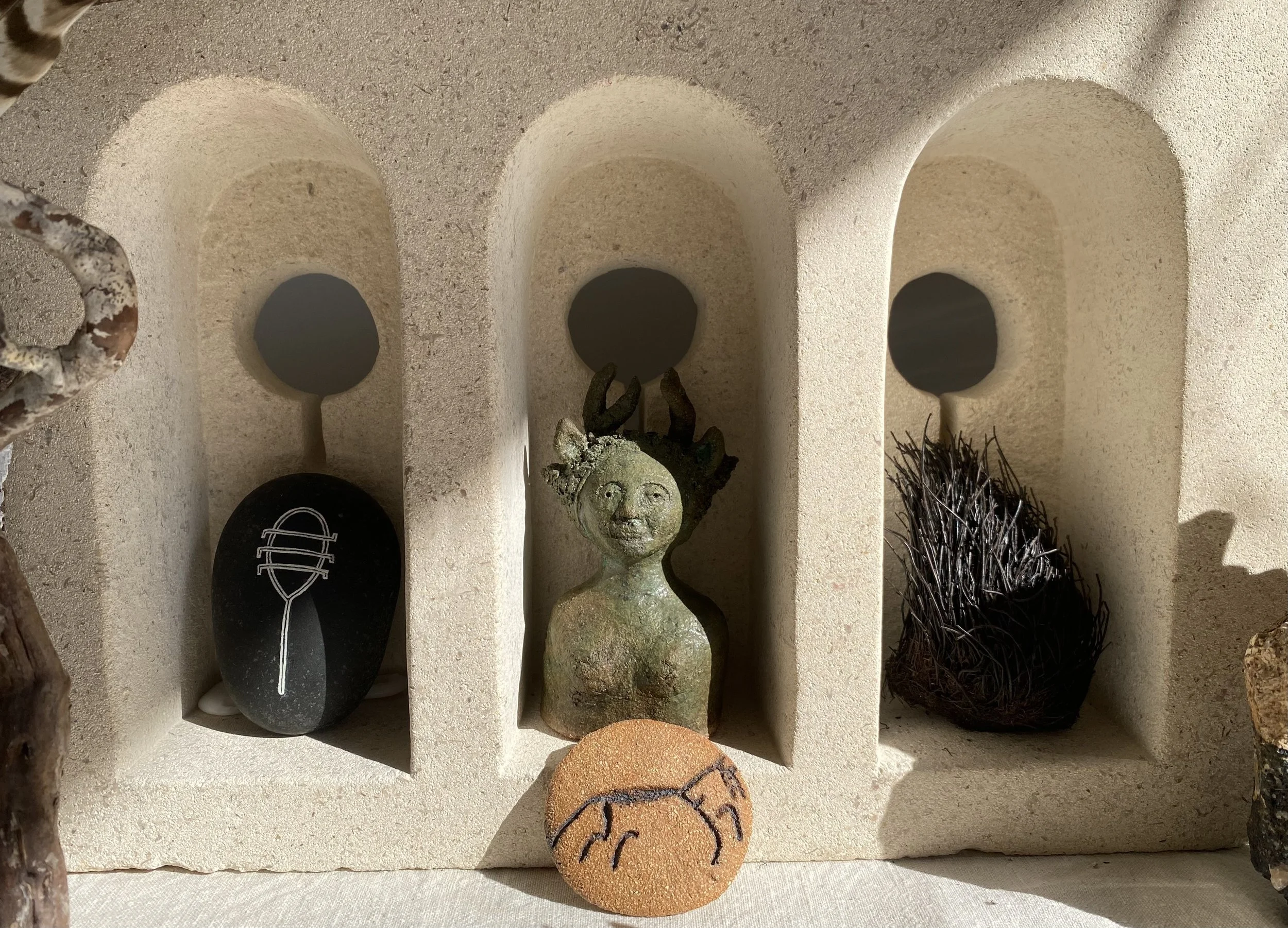 A display of various small rocks, a clay face sculpture, and a painted round stone, arranged in a case with arched compartments.