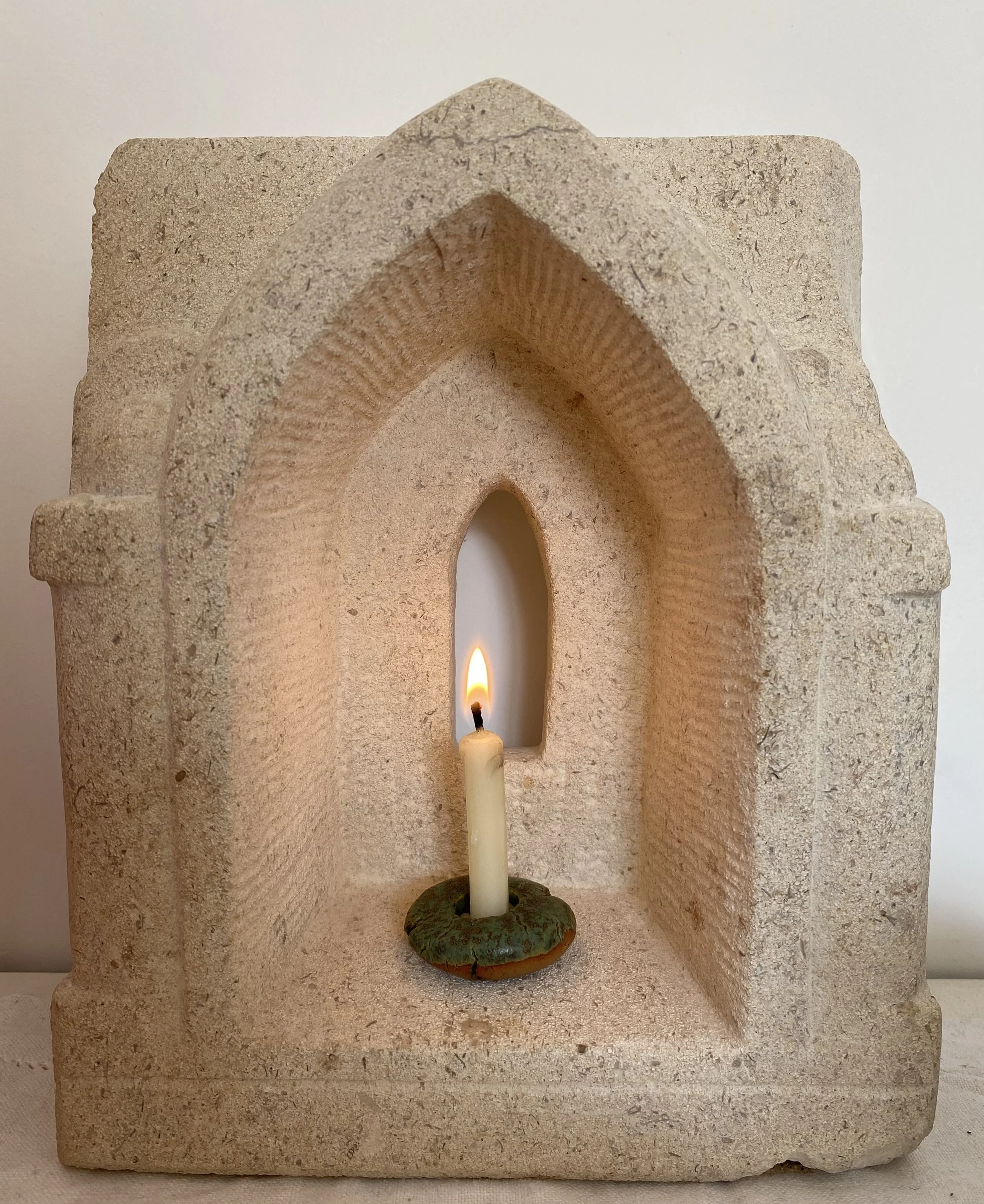 A carved stone chapel decorative structure with thin candle in a greenish-brown holder at the center.