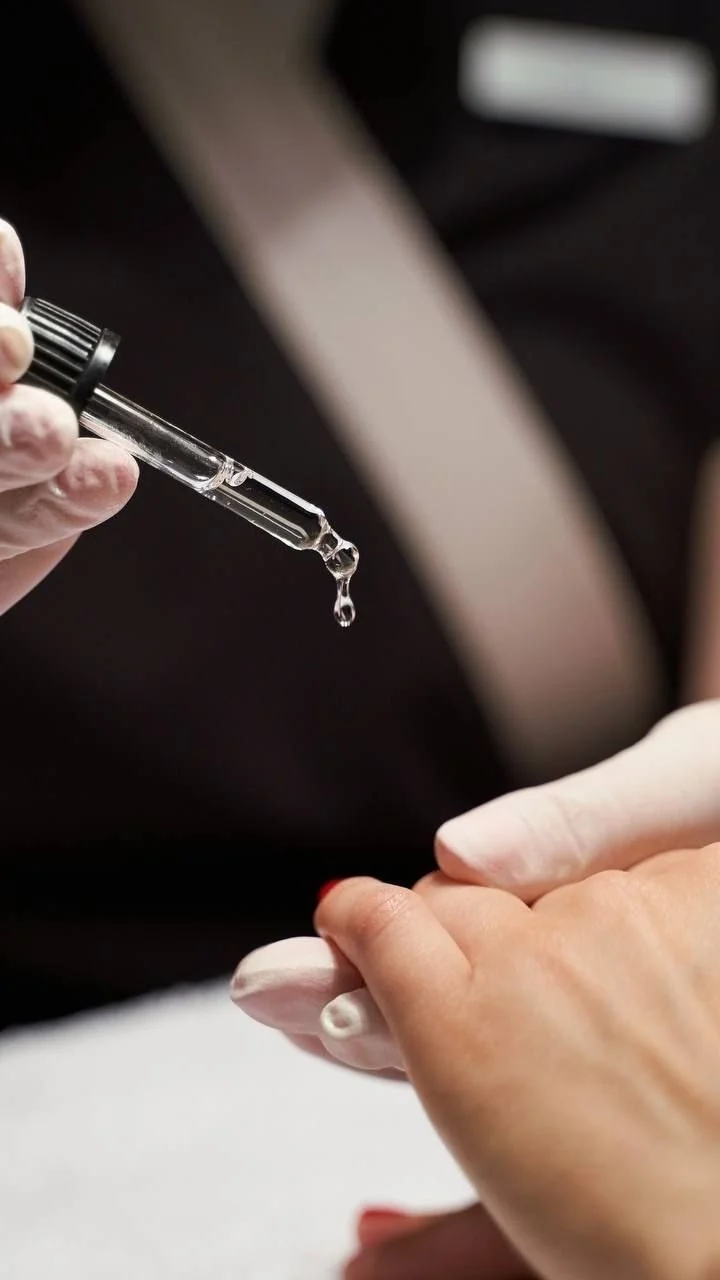 Close-up of a person's hand receiving a clear liquid from a dropper, possibly during a medical or cosmetic procedure.