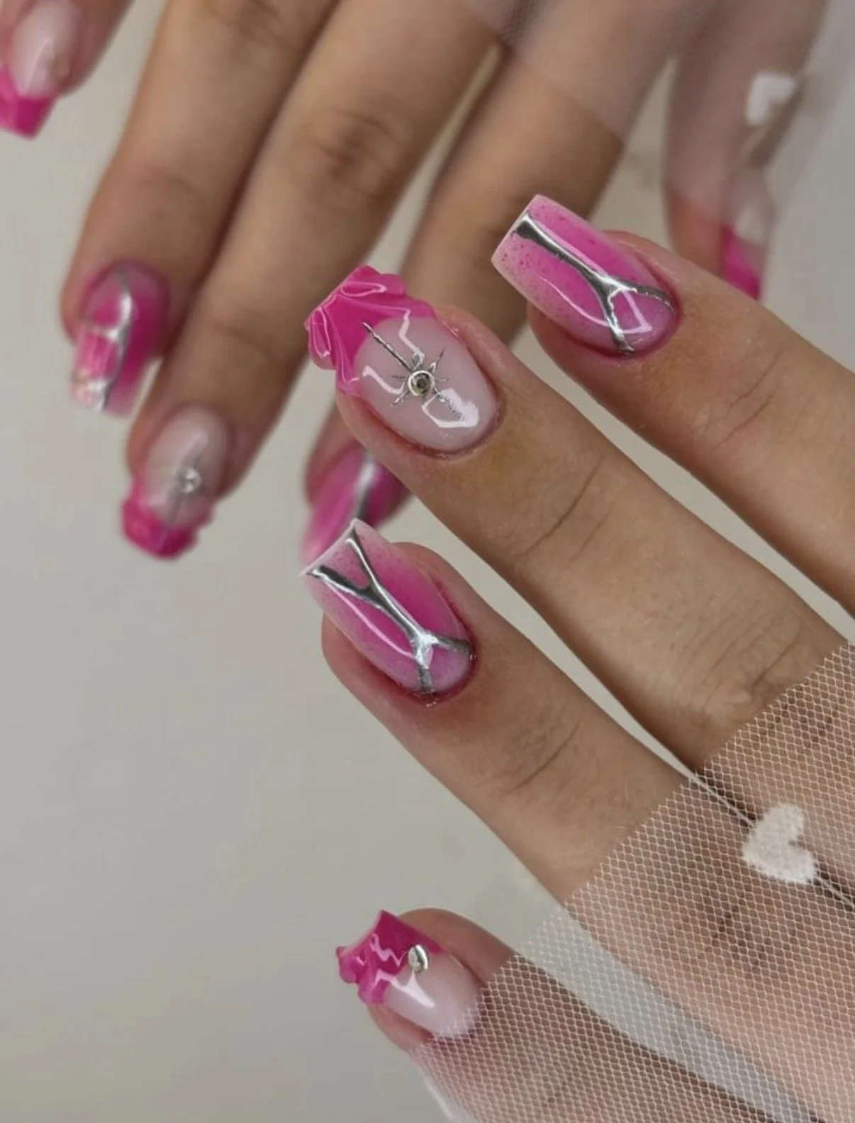 Close-up of hands with pink and white marble nail art, decorated with small silver charms, and sheer mesh glove with white heart detail.