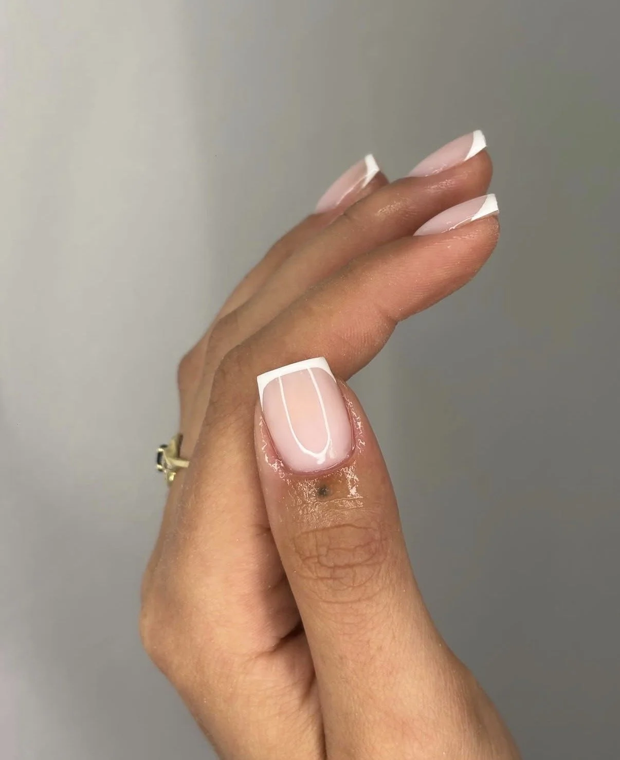 Close-up of a hand with a French manicure, showing a white tip on a pale pink nail, against a plain background.