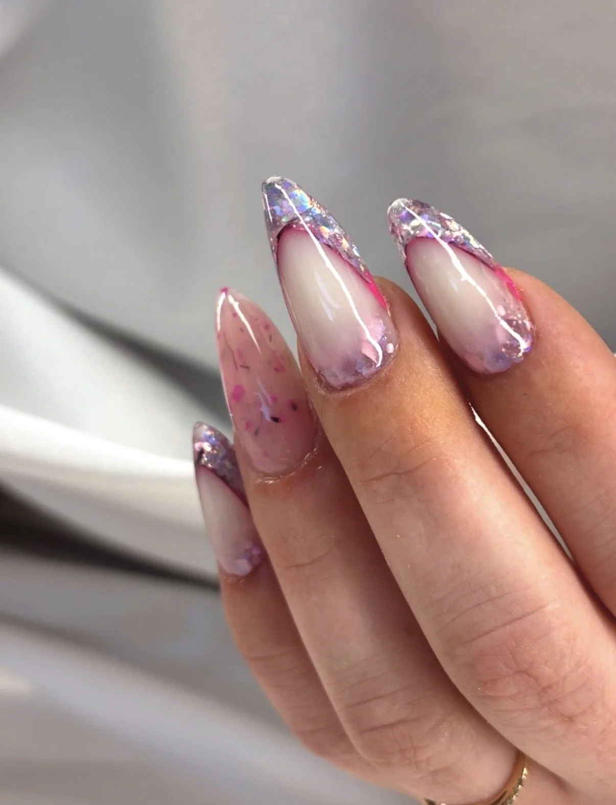 Close-up of a hand with long, pointed nails decorated with pink, white, and iridescent glitter, and a marbled pink design.