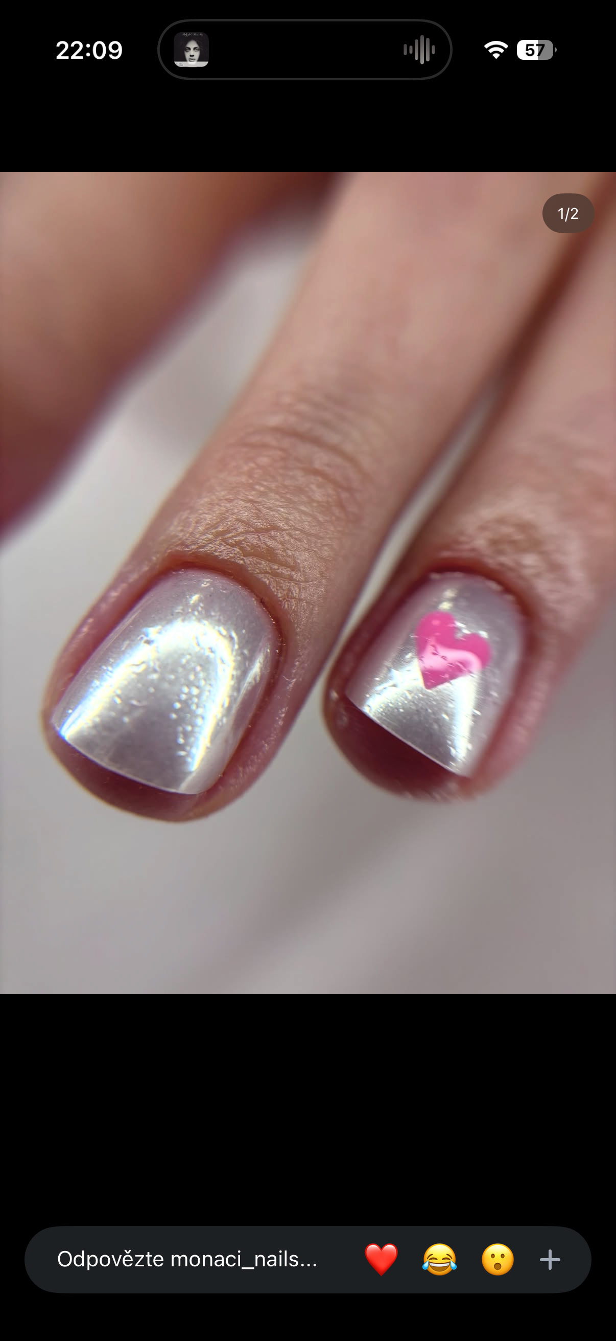 Close-up of two fingers with silver metallic nail polish, one nail decorated with a pink heart-shaped sticker.