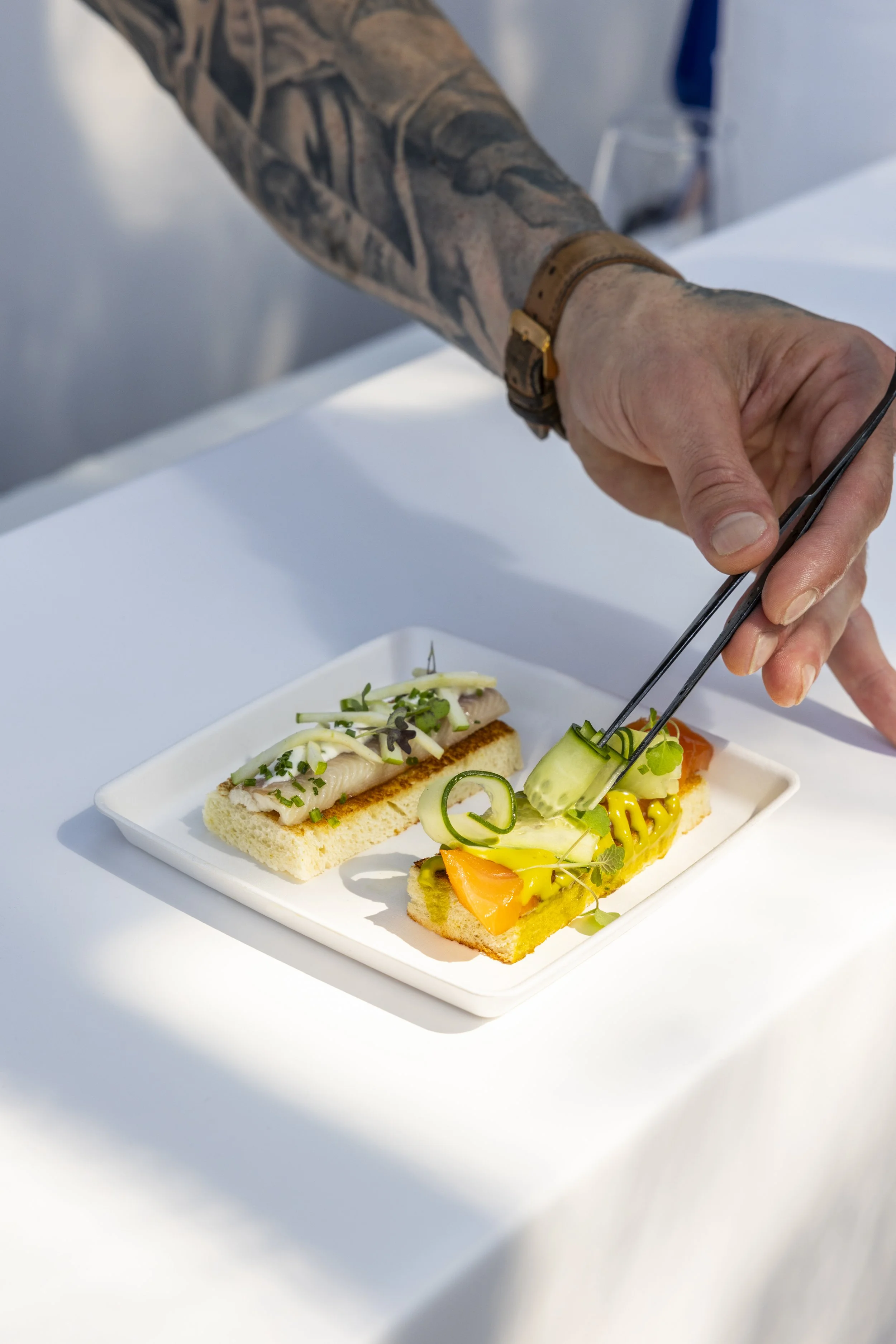 Verschillende kleine open sandwiches met vis, groenten en garnering op een witte schaal