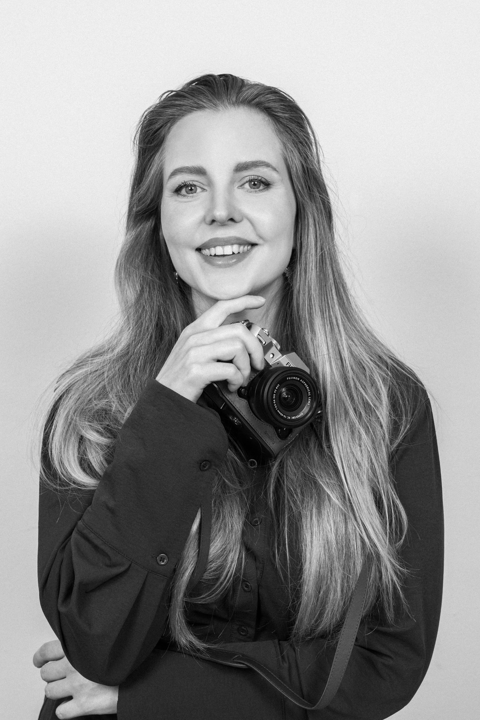 Portret van een lachende vrouw met lang haar, die een camera vasthoudt, in zwart-wit foto.