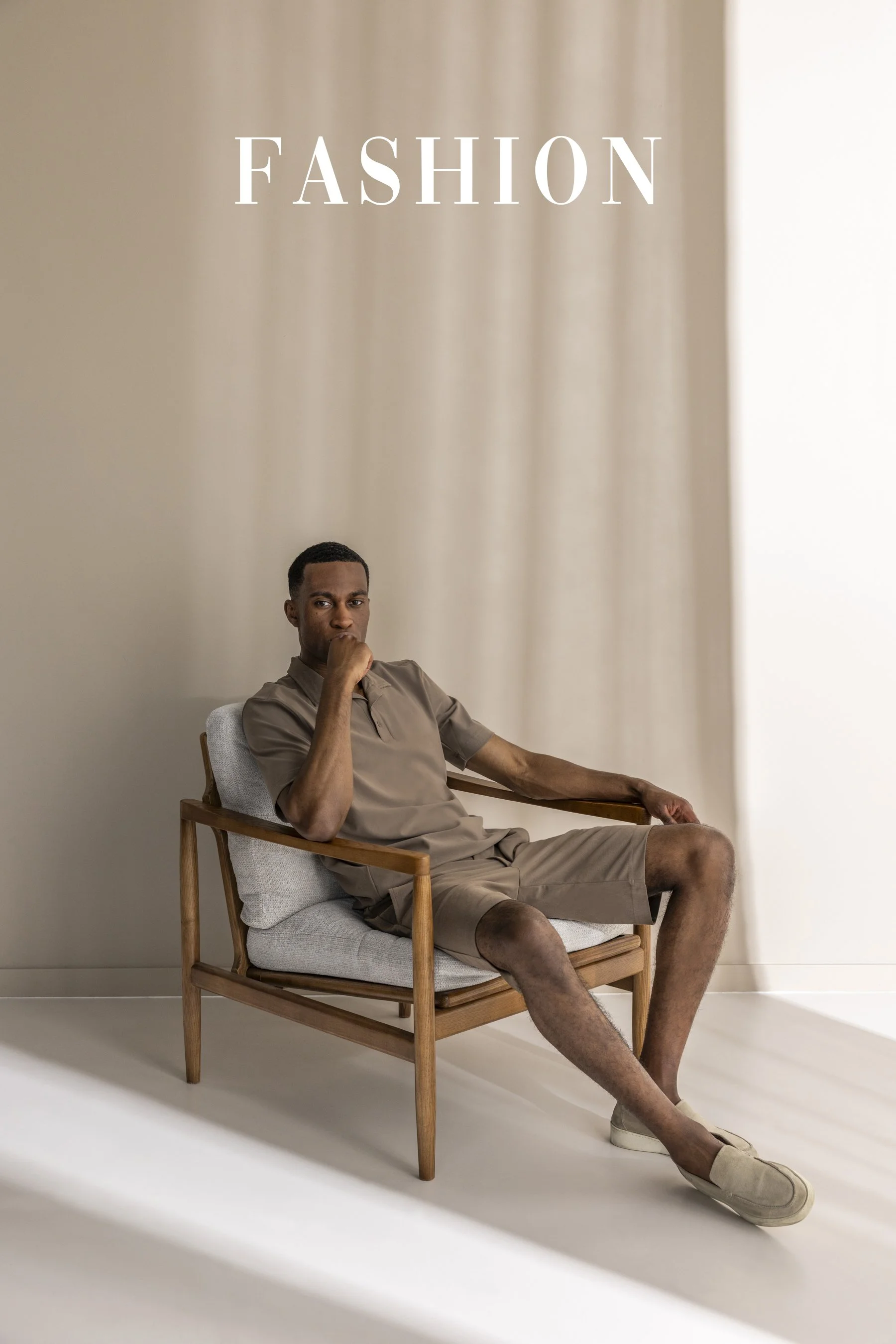 Man zit ontspannen op een houten stoel met lichte bekleding, gekleed in beige sportkleding, met een neutrale achtergrond en de tekst 'Fashion' erboven.