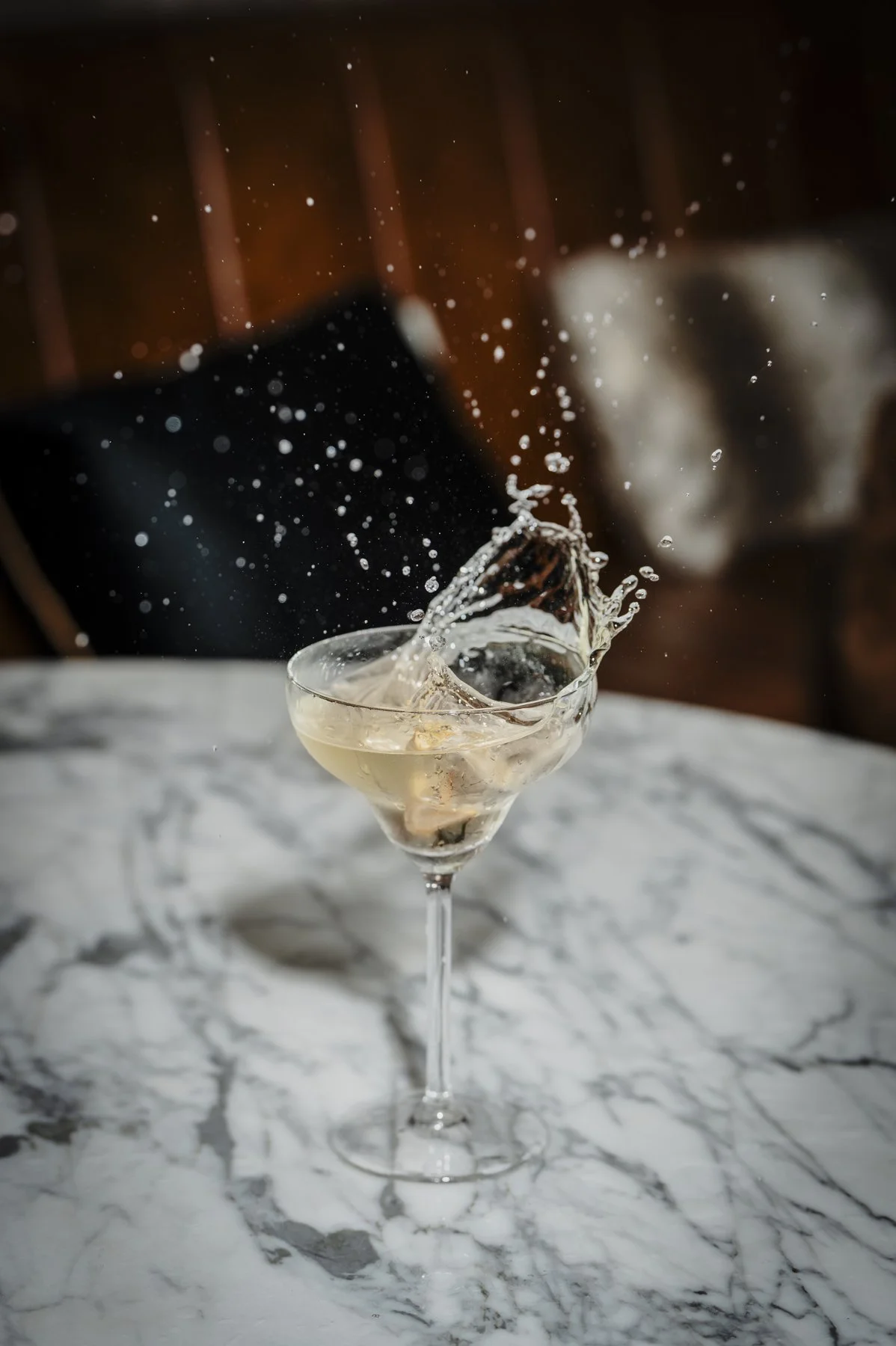 Een glas met champagne wordt geschud en de vloeistof spat eruit, geplaatst op een witte marmeren tafel.