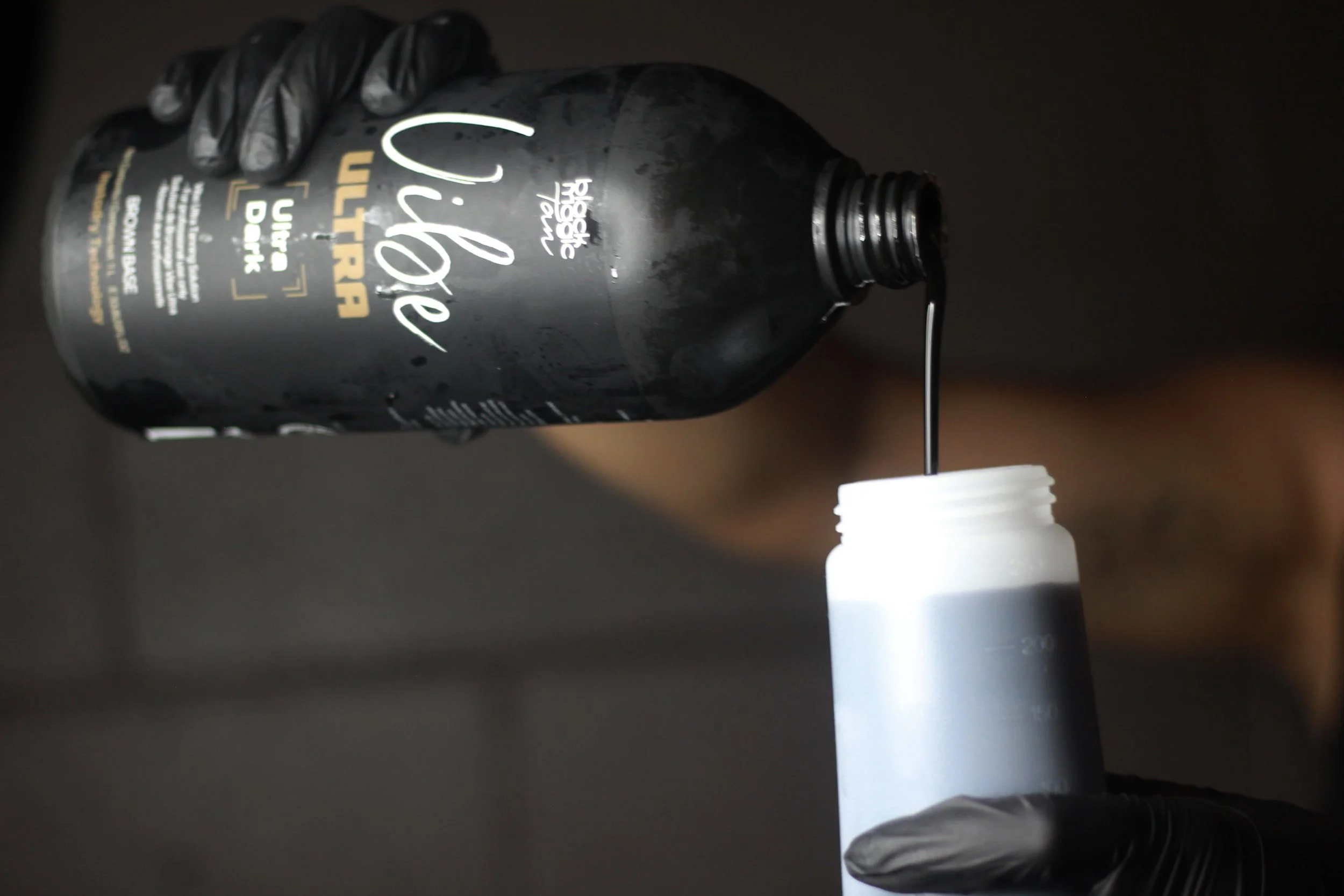 A person wearing black gloves pouring black liquid from a bottle labeled 'Cárepo Ultra' into a white measuring cup.