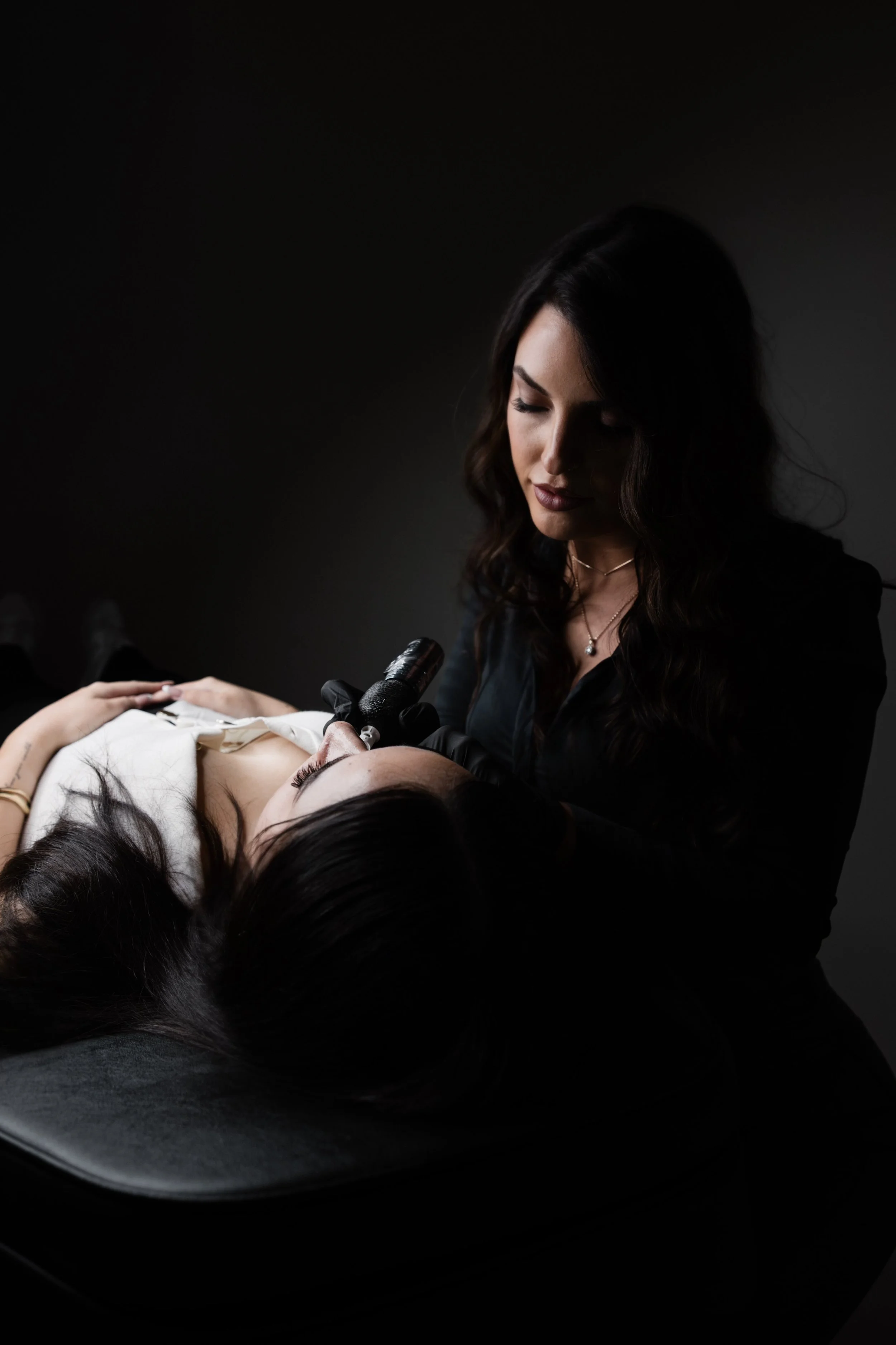 Beauty technician performing a cosmetic procedure on a woman lying on a treatment bed.