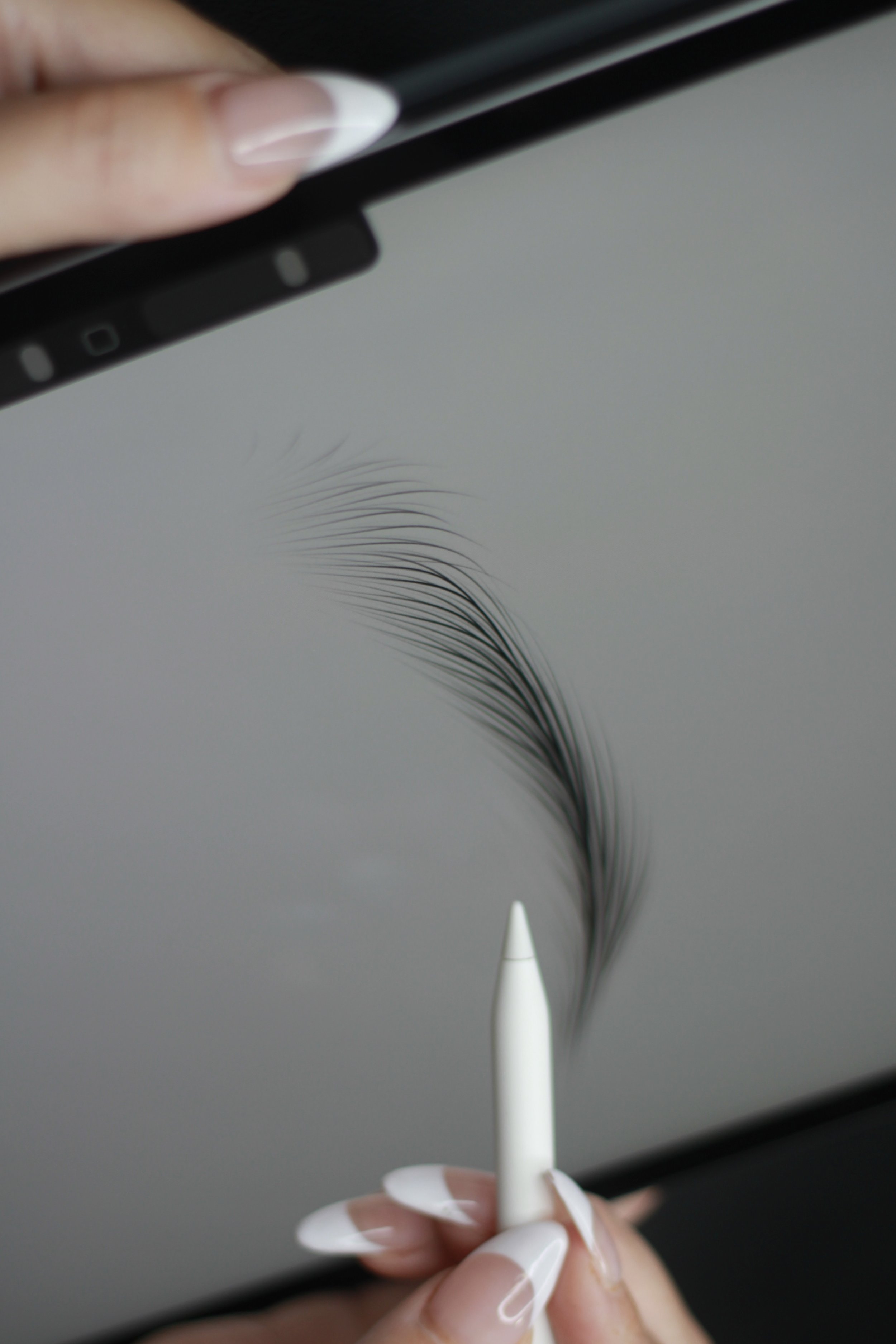 A person with well-manicured nails holds a white marker and draws on a tablet screen, creating a detailed digital drawing of eyelashes.