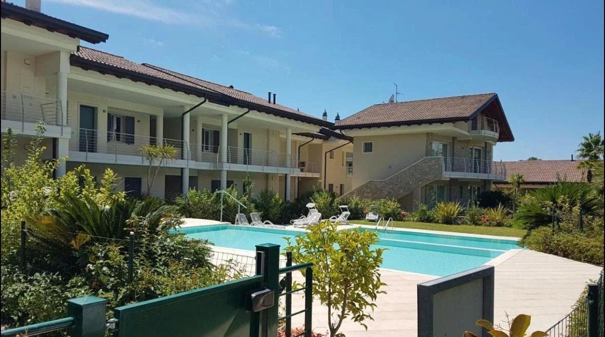 Modern residential complex with a swimming pool surrounded by lounge chairs and lush greenery.