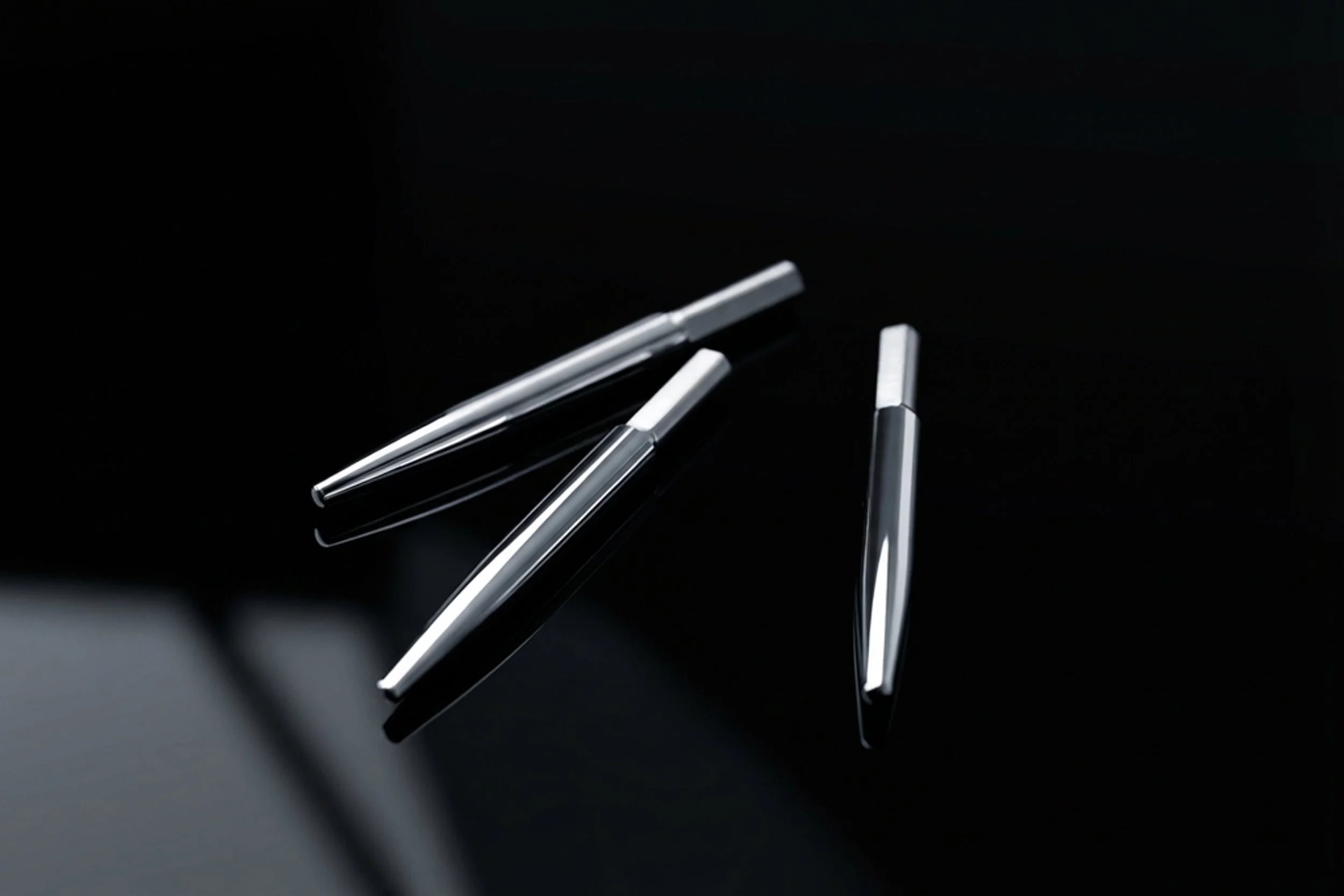 Drei silberne Kugelschreiber auf schwarzem Hintergrund, einer liegt senkrecht, die anderen beiden liegen schräg.