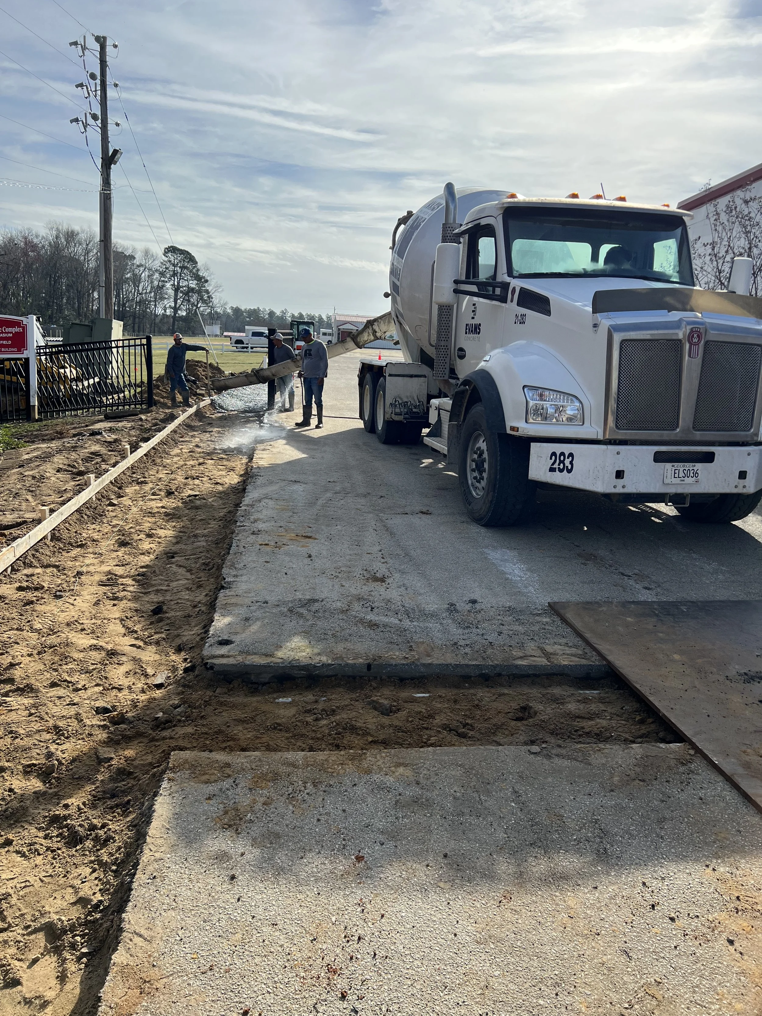 Construction workers pour concrete from a mixer truck onto a sidewalk during roadwork.