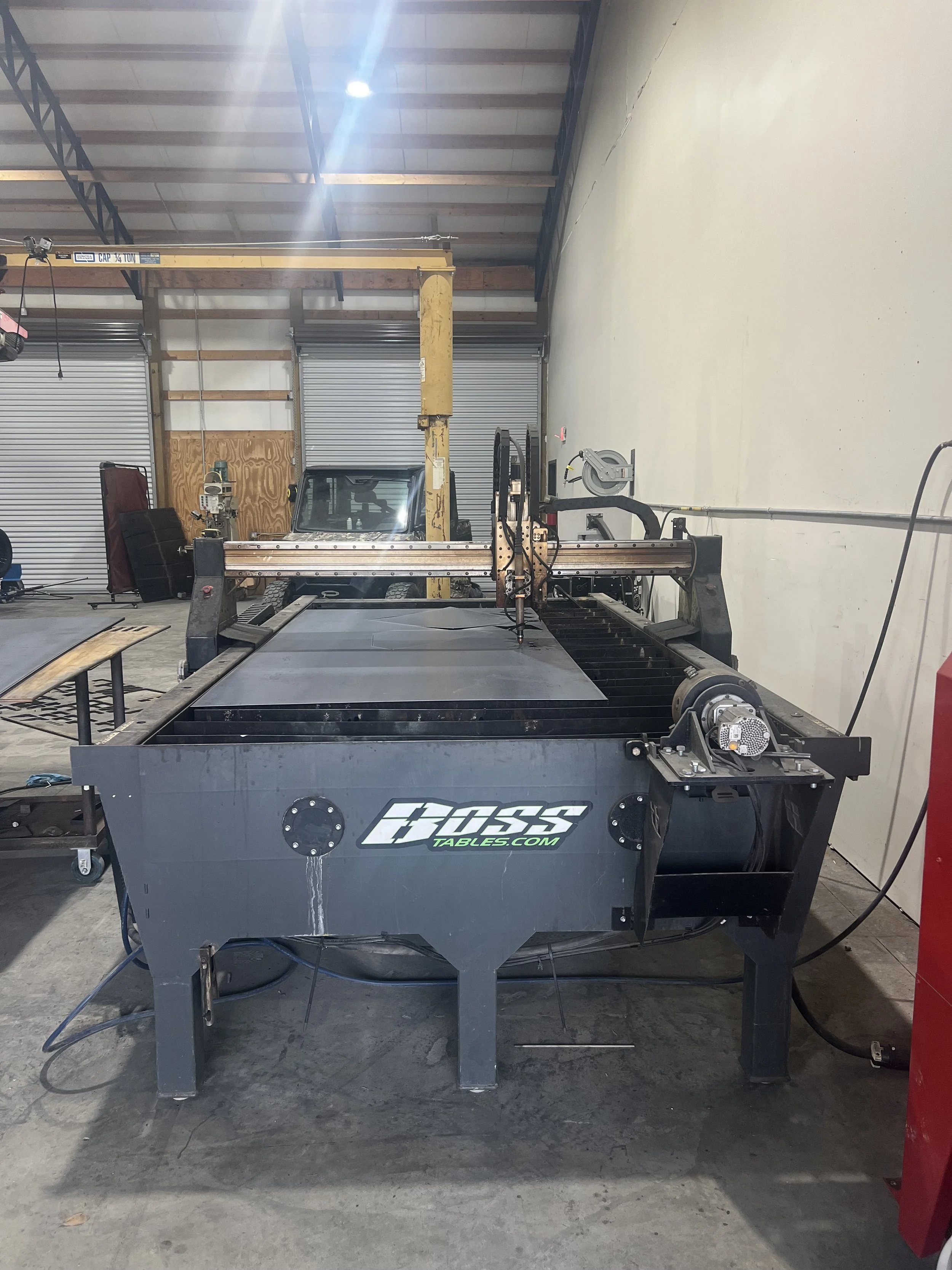 Industrial CNC plasma cutting machine with a cutting arm on a large metal table in a workshop.