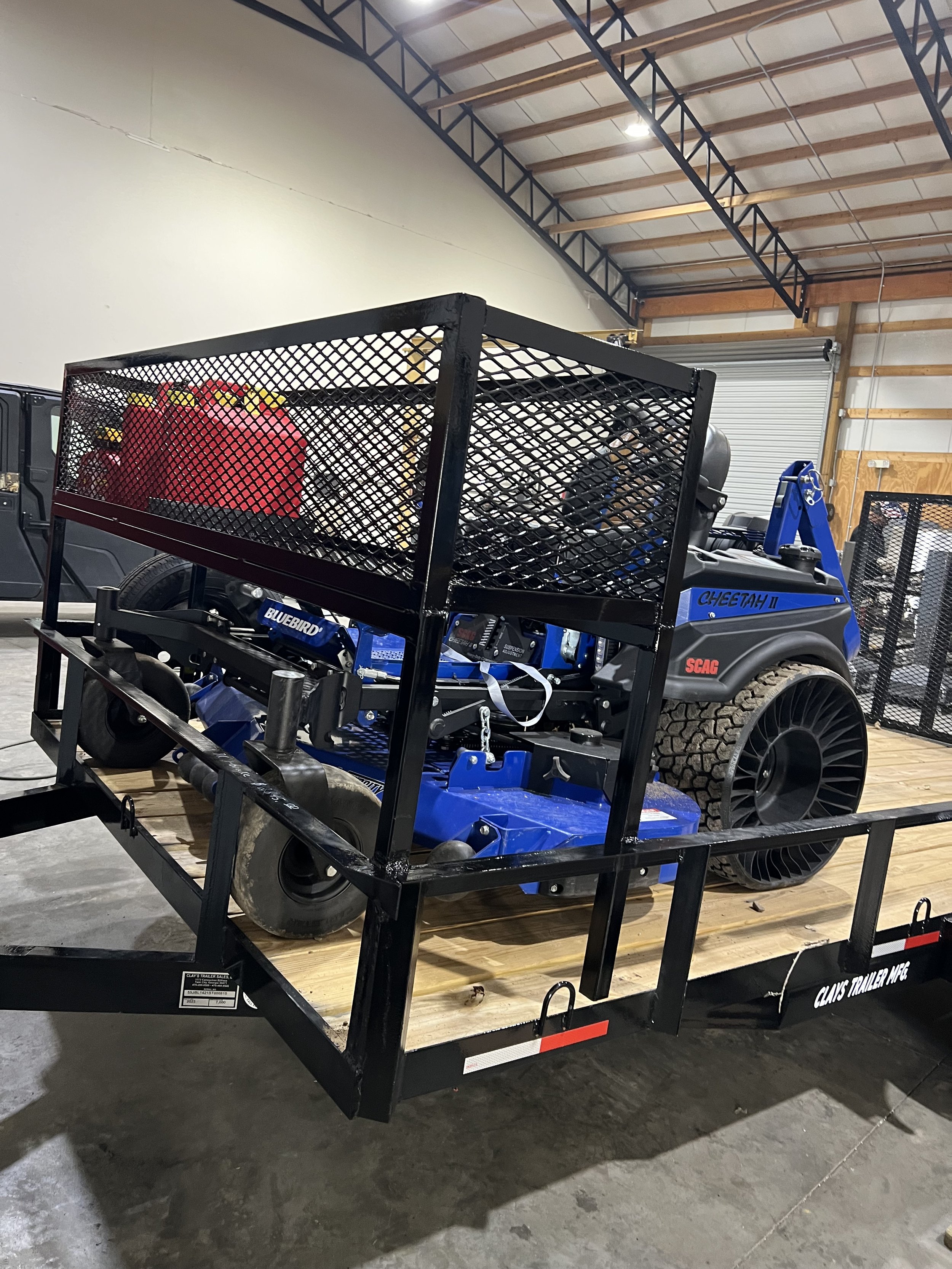 A flatbed trailer with a blue force machine and safety equipment, parked inside a warehouse with a high ceiling and metal beams.