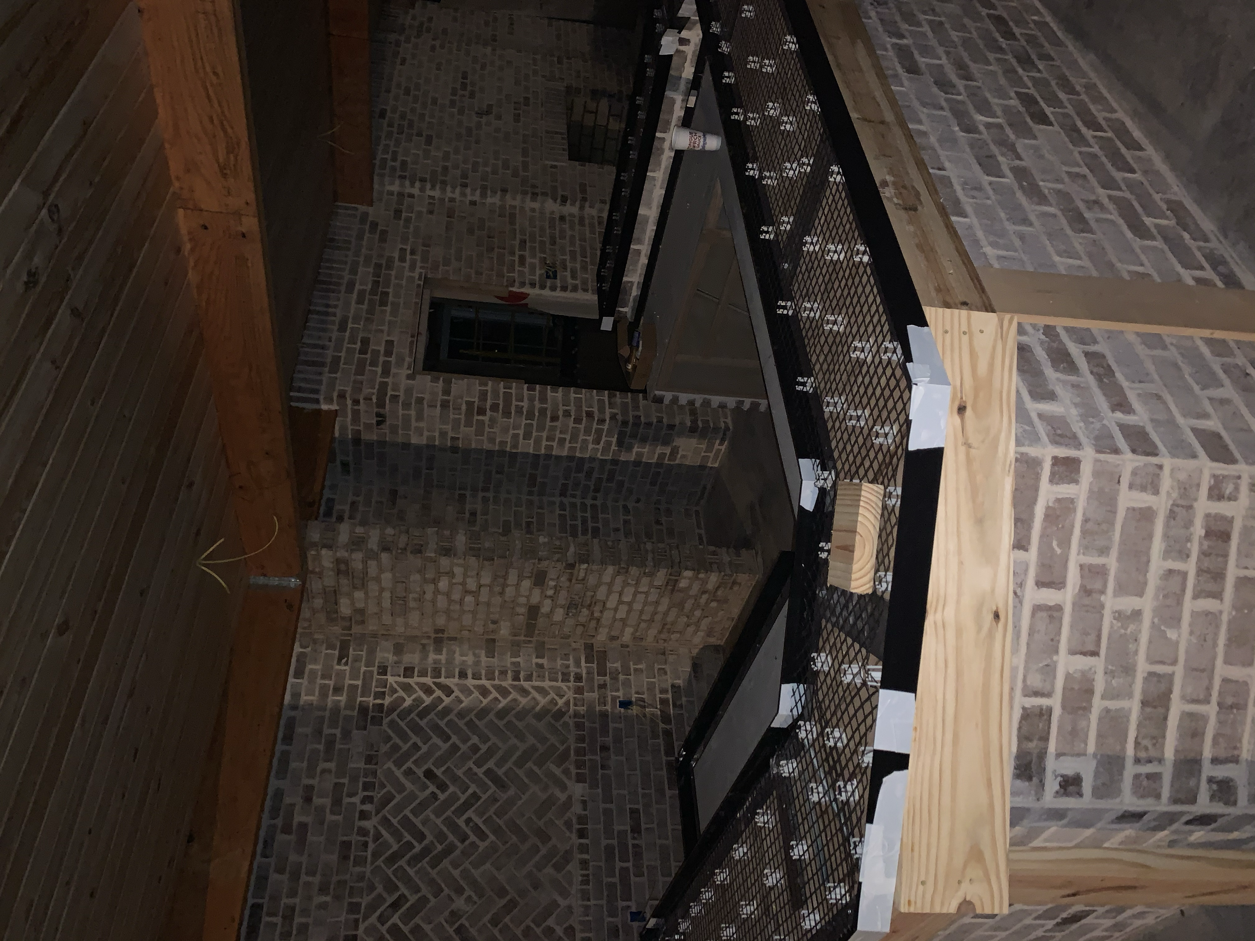 Unfinished bartop made of wood and black metal grid in a room with brick walls and wooden accents.